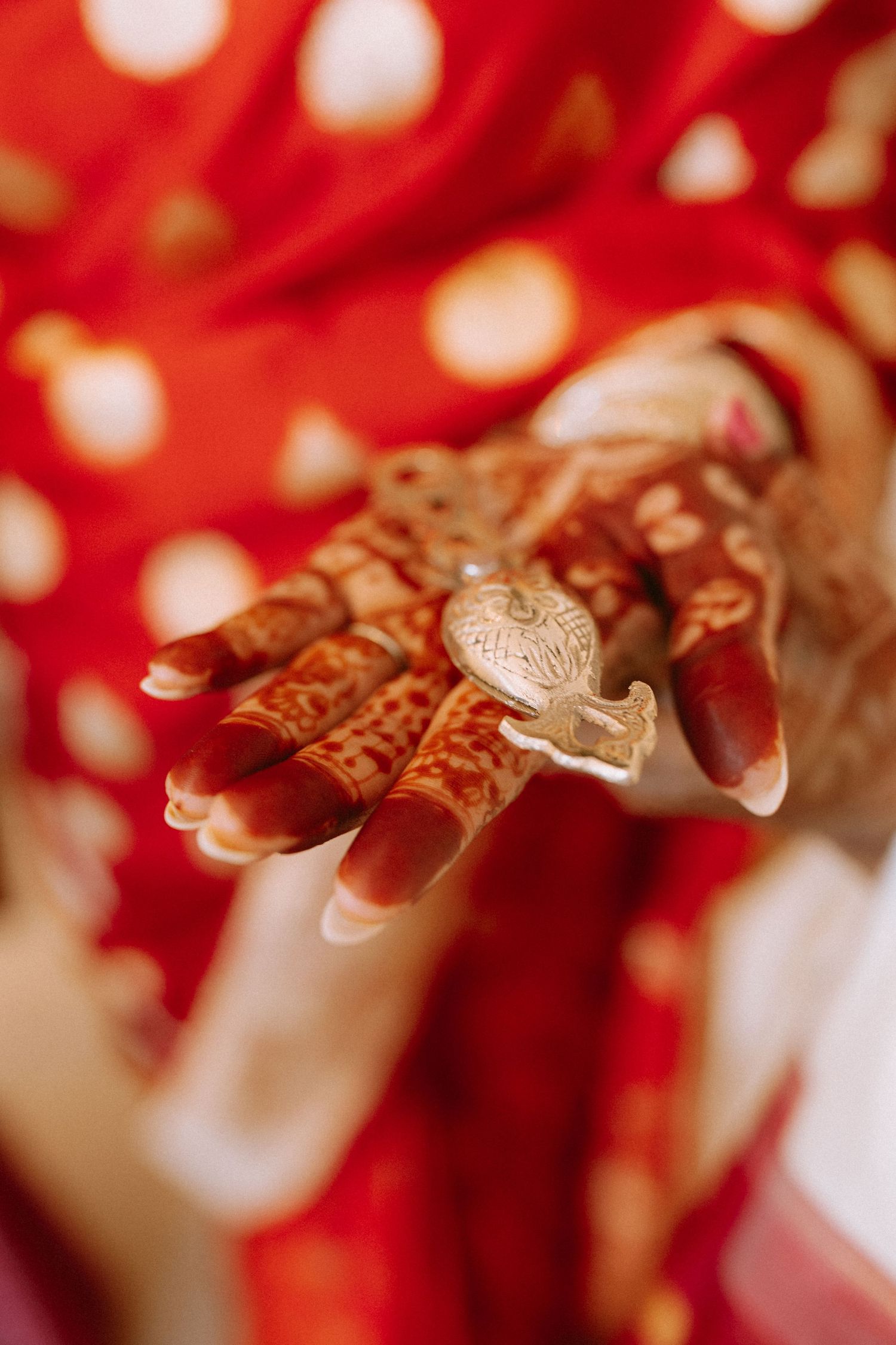 Intricate henna designs adorning hands with traditional bangles against a red background.