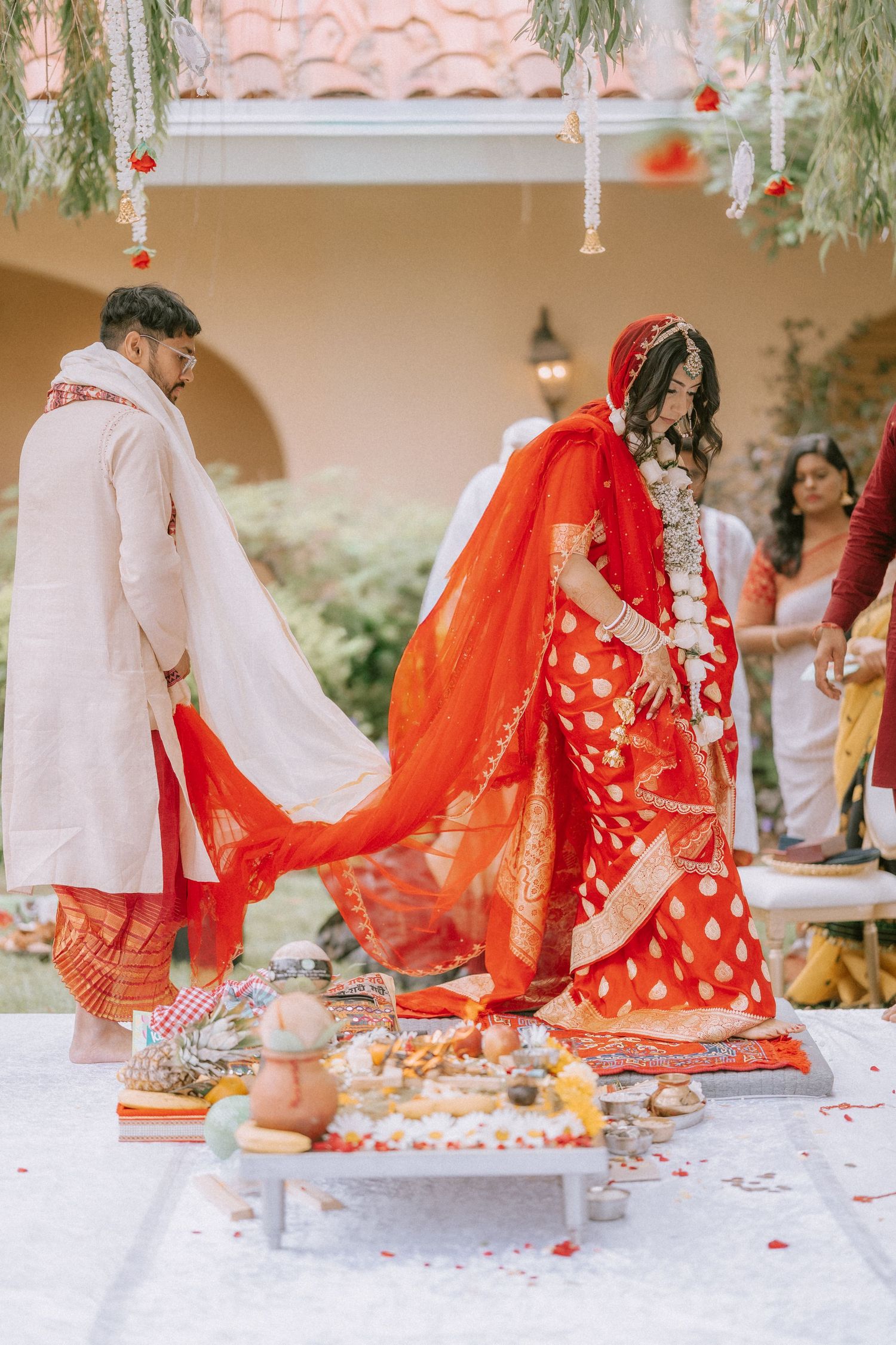 Traditional Indian wedding ceremony showing bride and groom performing sacred rituals on decorated mandap with red decor.