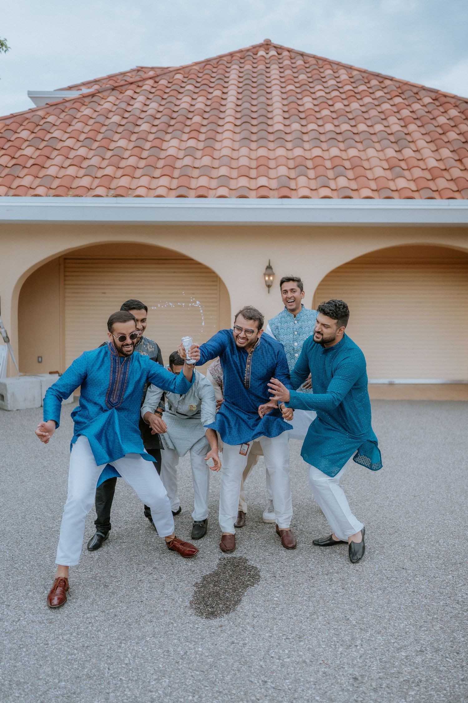 Group of friends in coordinated blue and white outfits posing playfully on concrete ground near Spanish-style building.