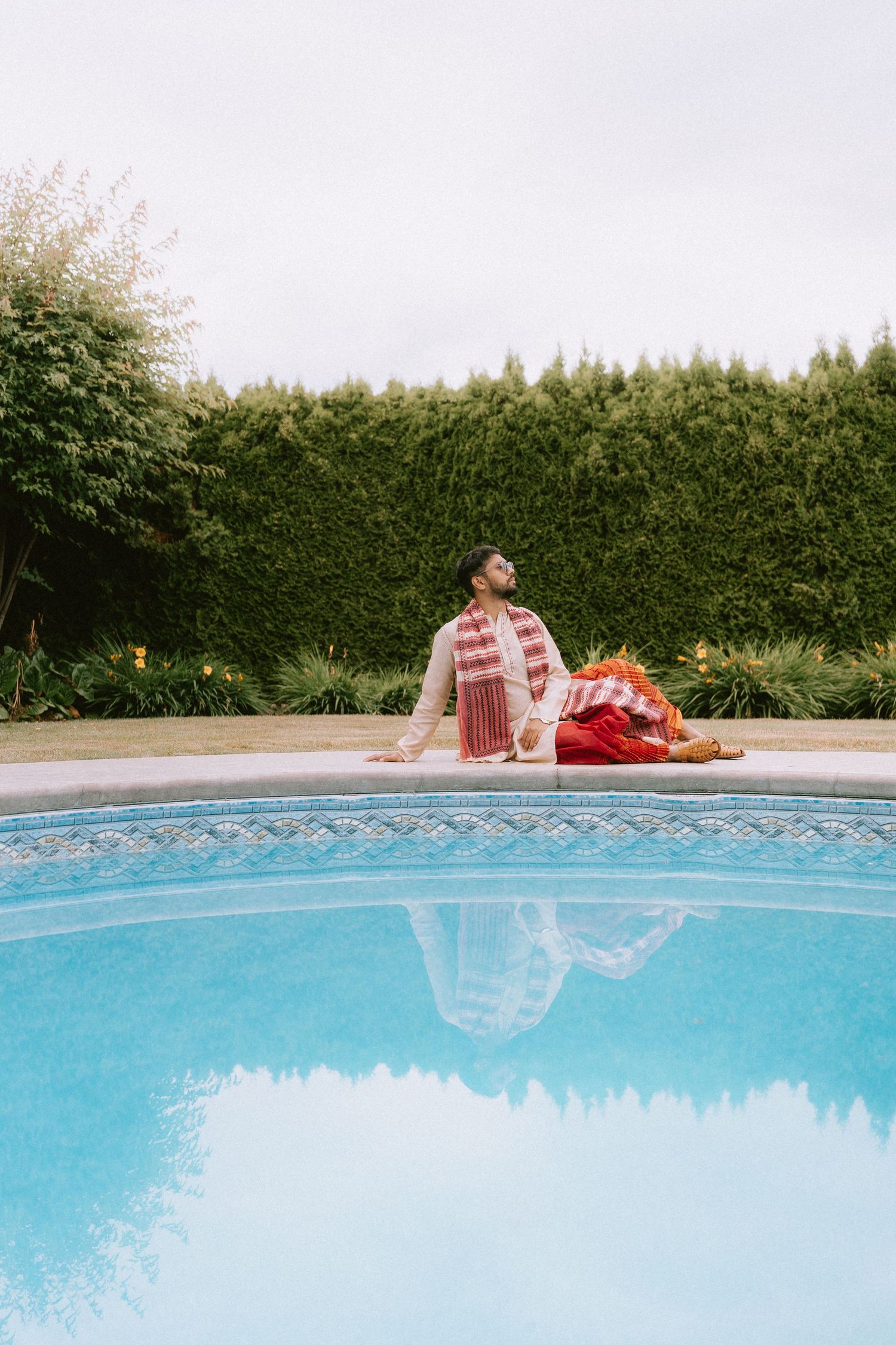 Split view photograph showing a person in red clothing reflected in a swimming pool's turquoise water.