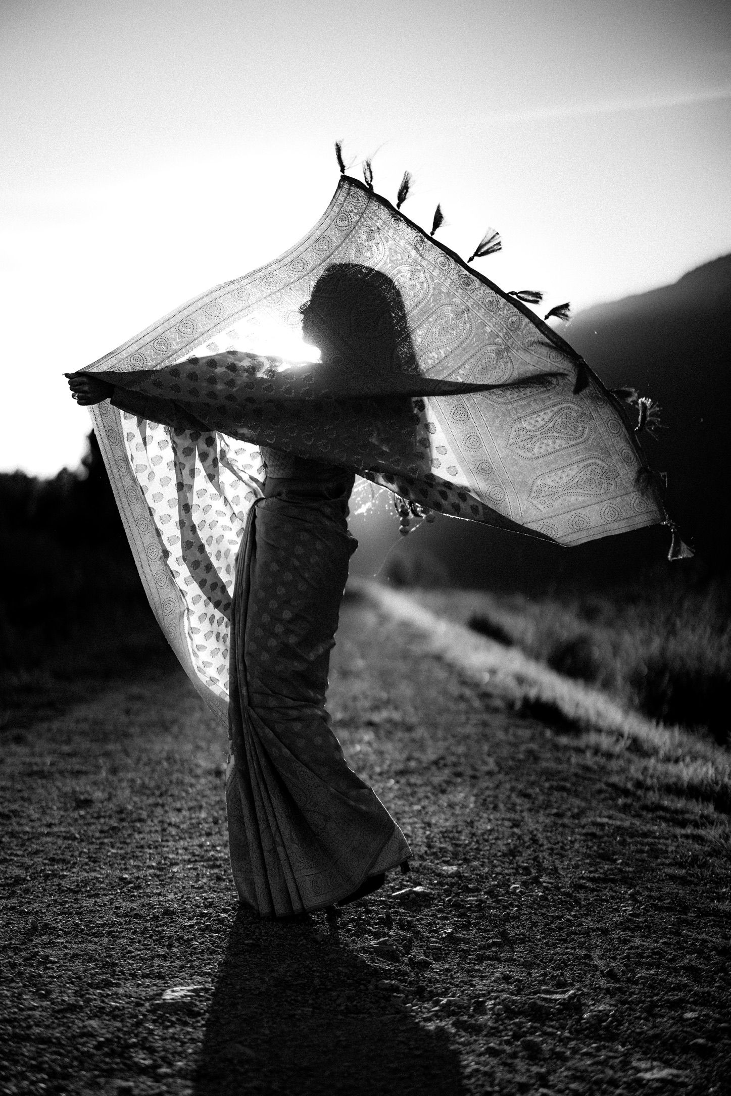 A silhouetted figure in a flowing dress twirls with fabric billowing in the wind against a moody black and white backdrop.