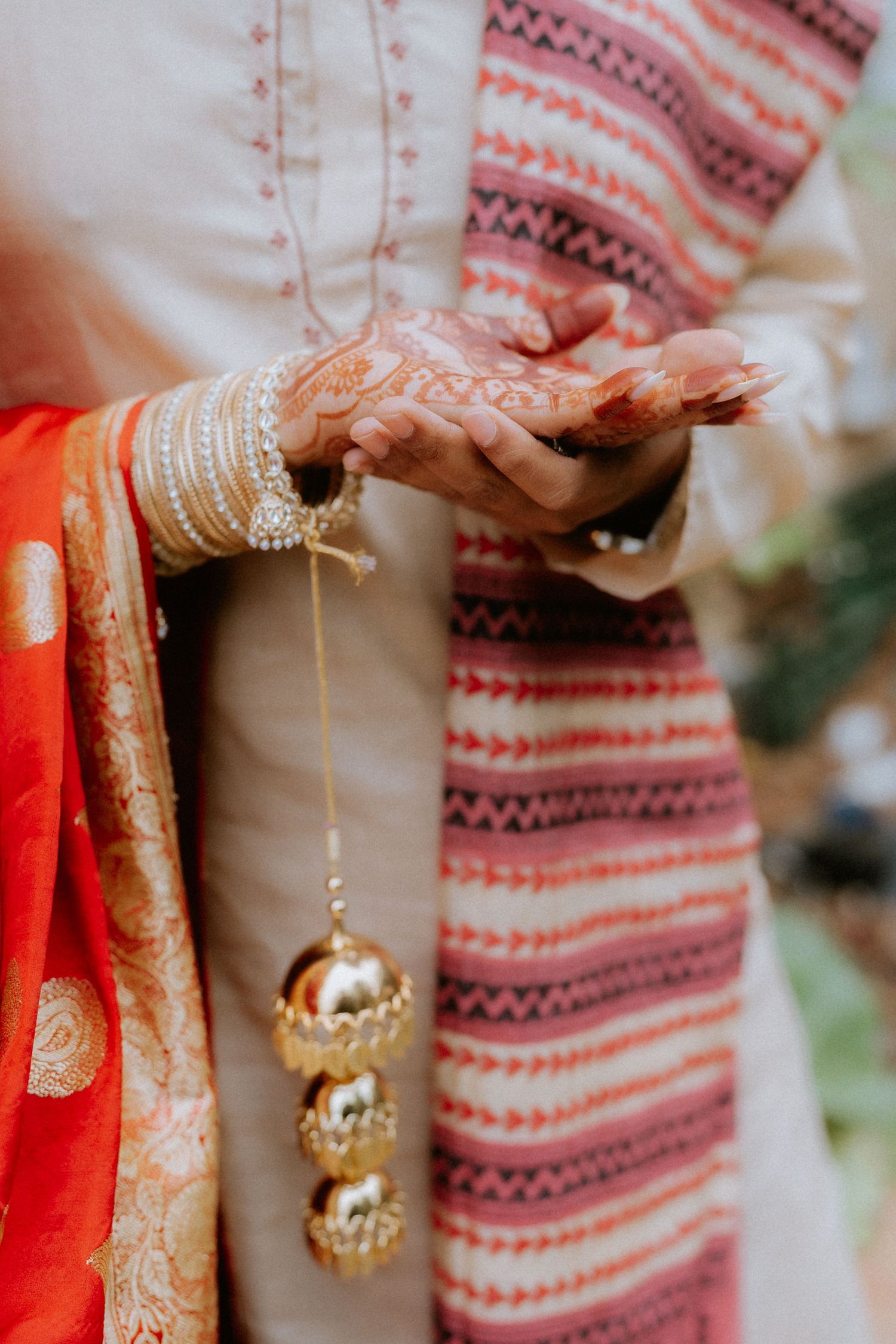 Close-up of traditional Indian bridal hands adorned with gold bangles, pearl jewelry and intricate henna designs.
