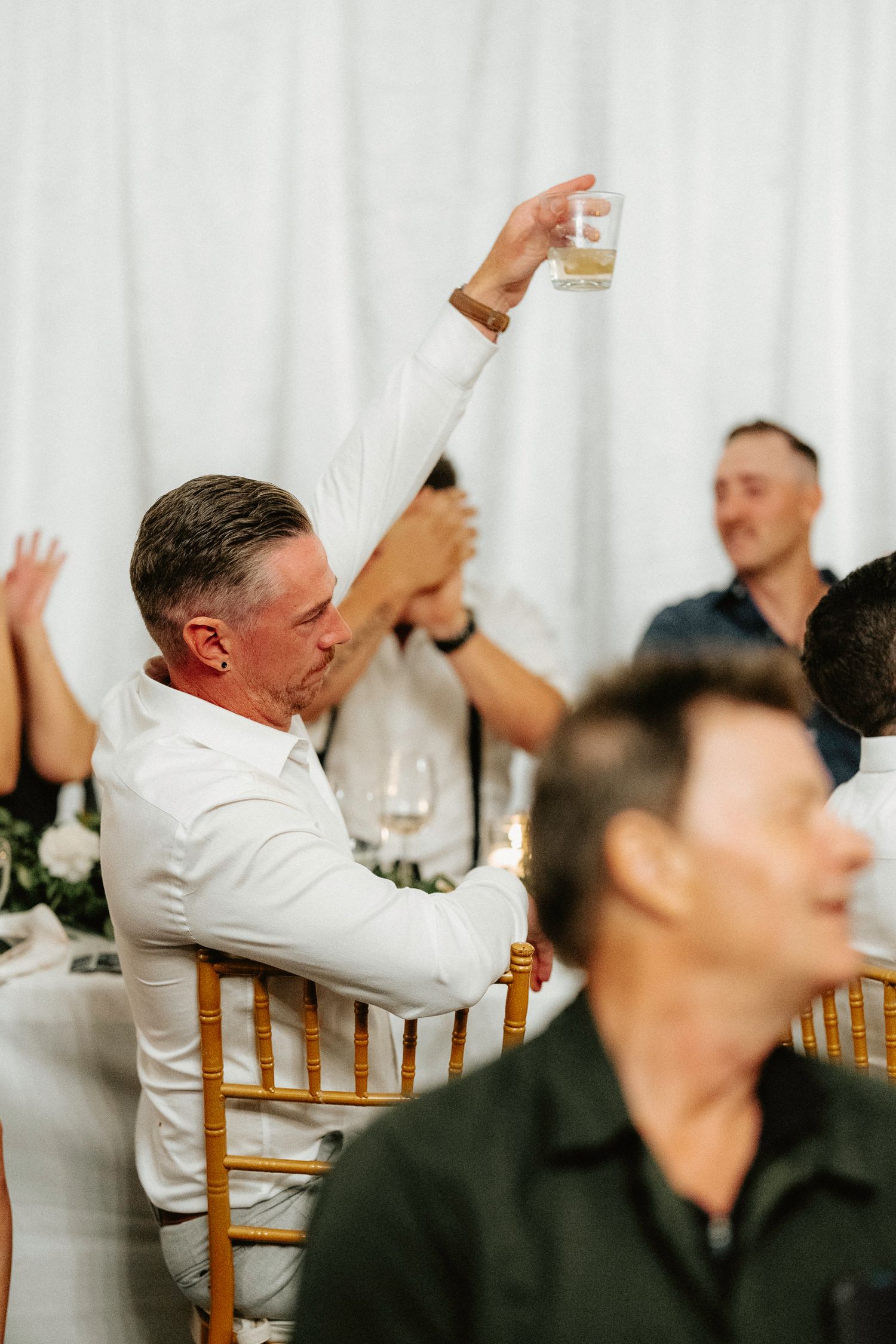 Wedding reception guests in formal attire raising glasses in celebration.