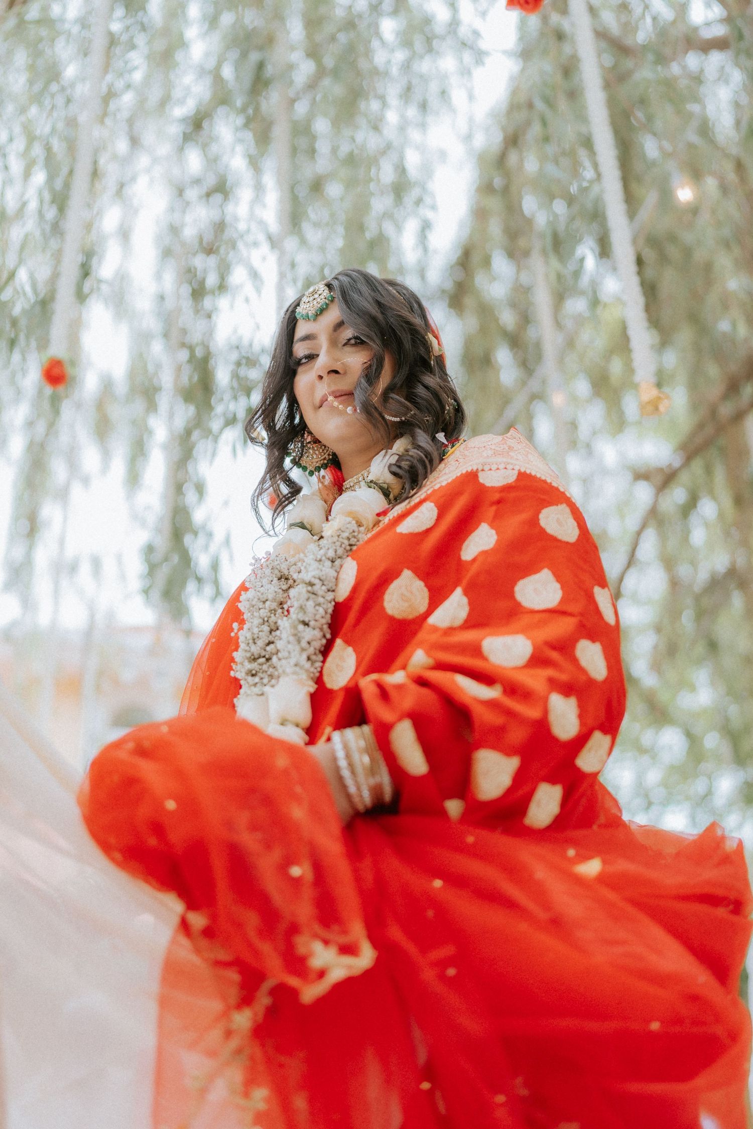 Person in flowing red and gold sari twirling gracefully against a backdrop of willow trees.