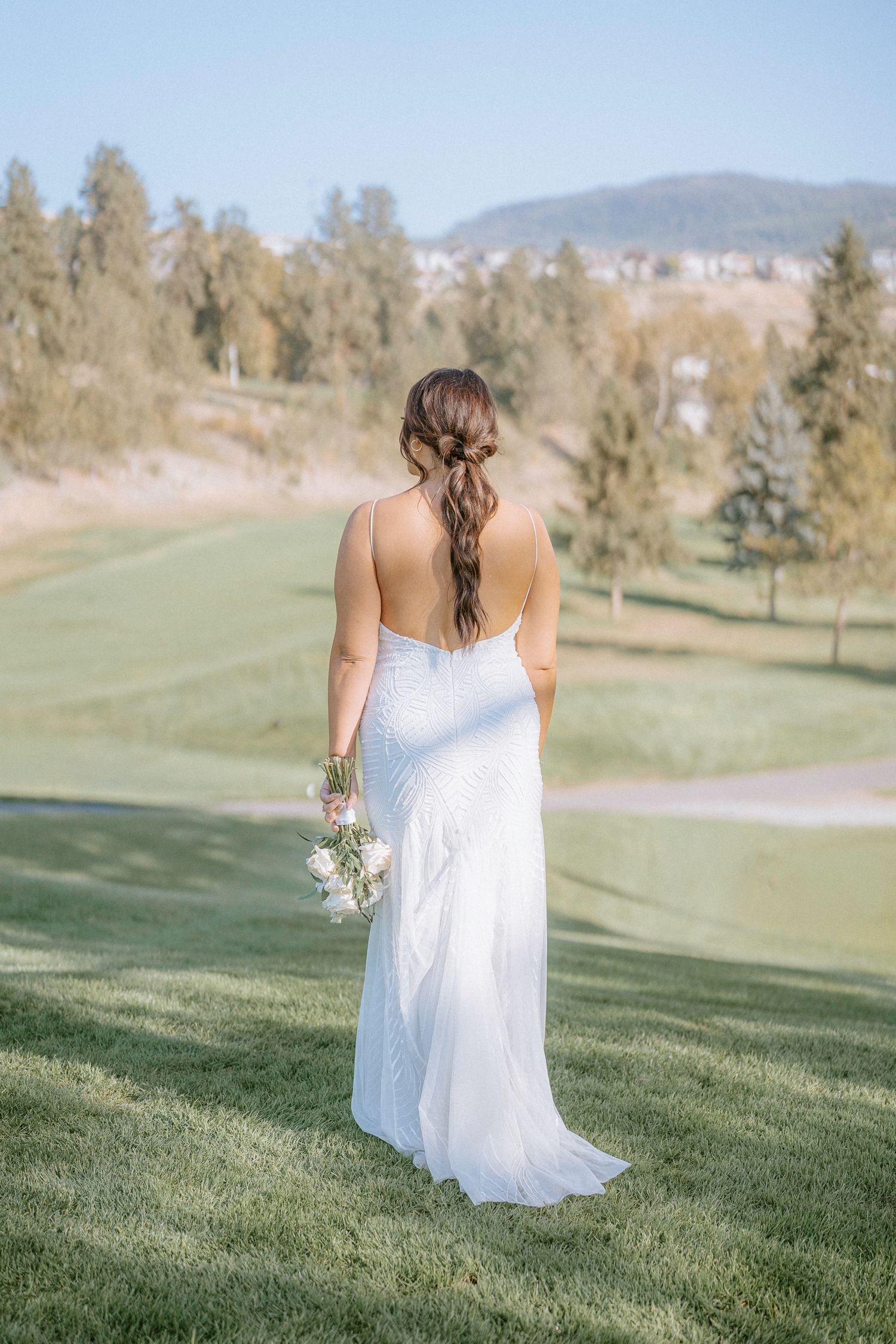 A white flowy dress against a green golf course landscape with mountains in the background.
