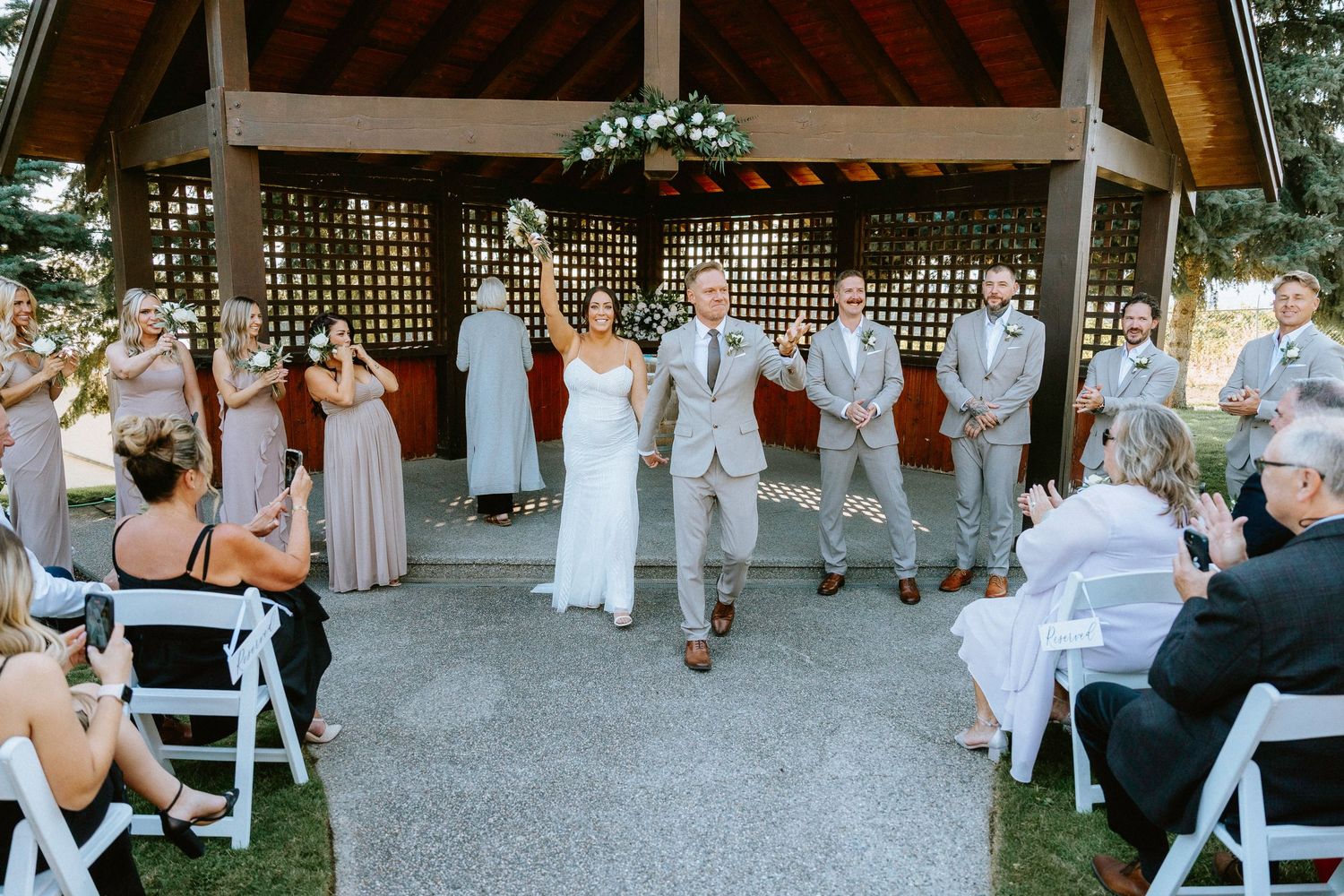 Wide panoramic shot of wedding guests mingling under a rustic pavilion during reception celebrations.