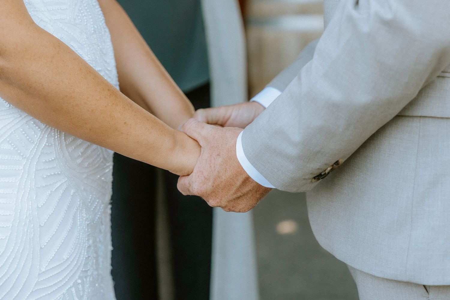 Close-up view of hands holding white wedding dress fabric showing delicate details and textures.