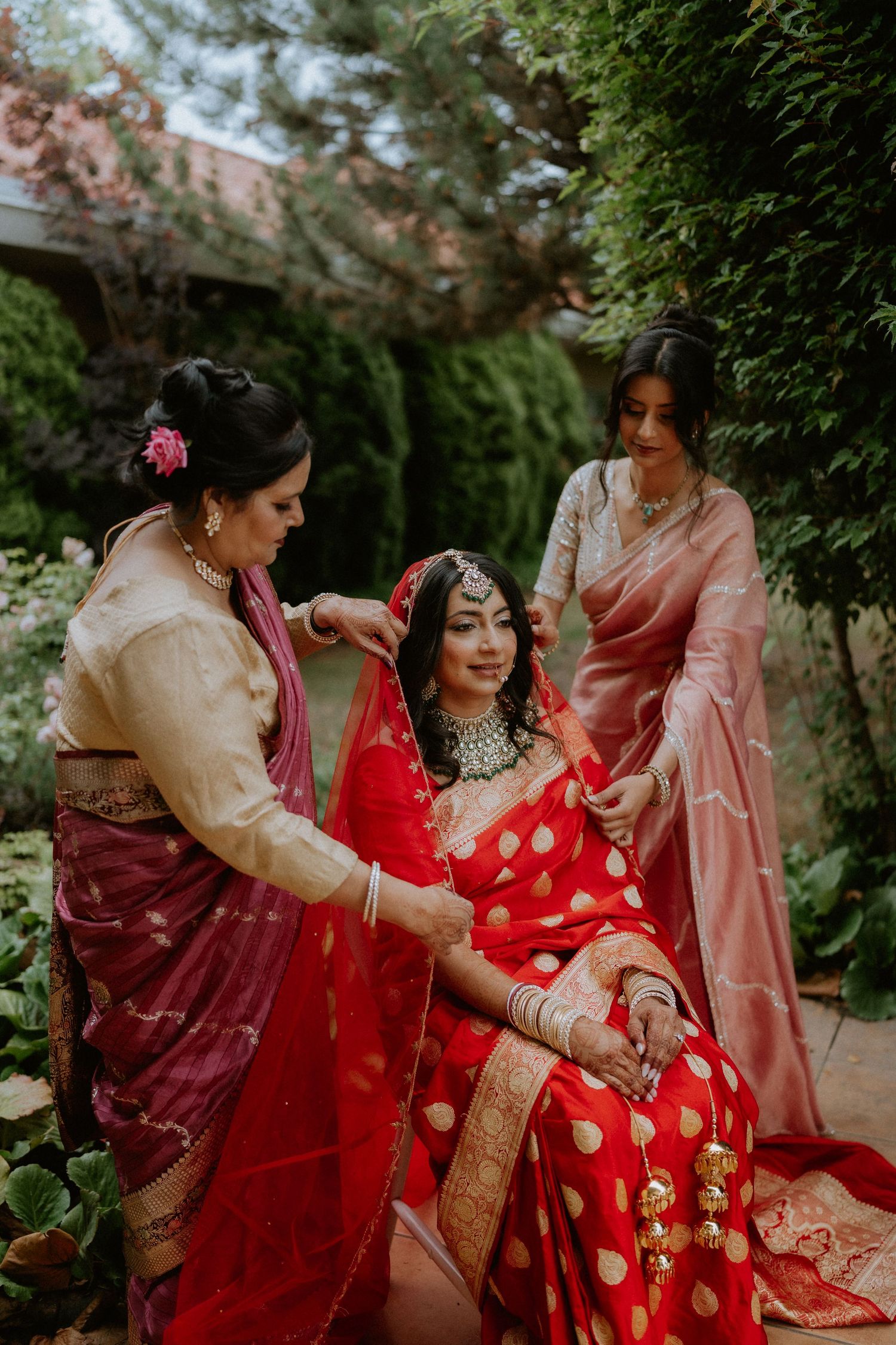 Traditional Indian wedding preparation scene with attendants helping arrange a red and gold sari.