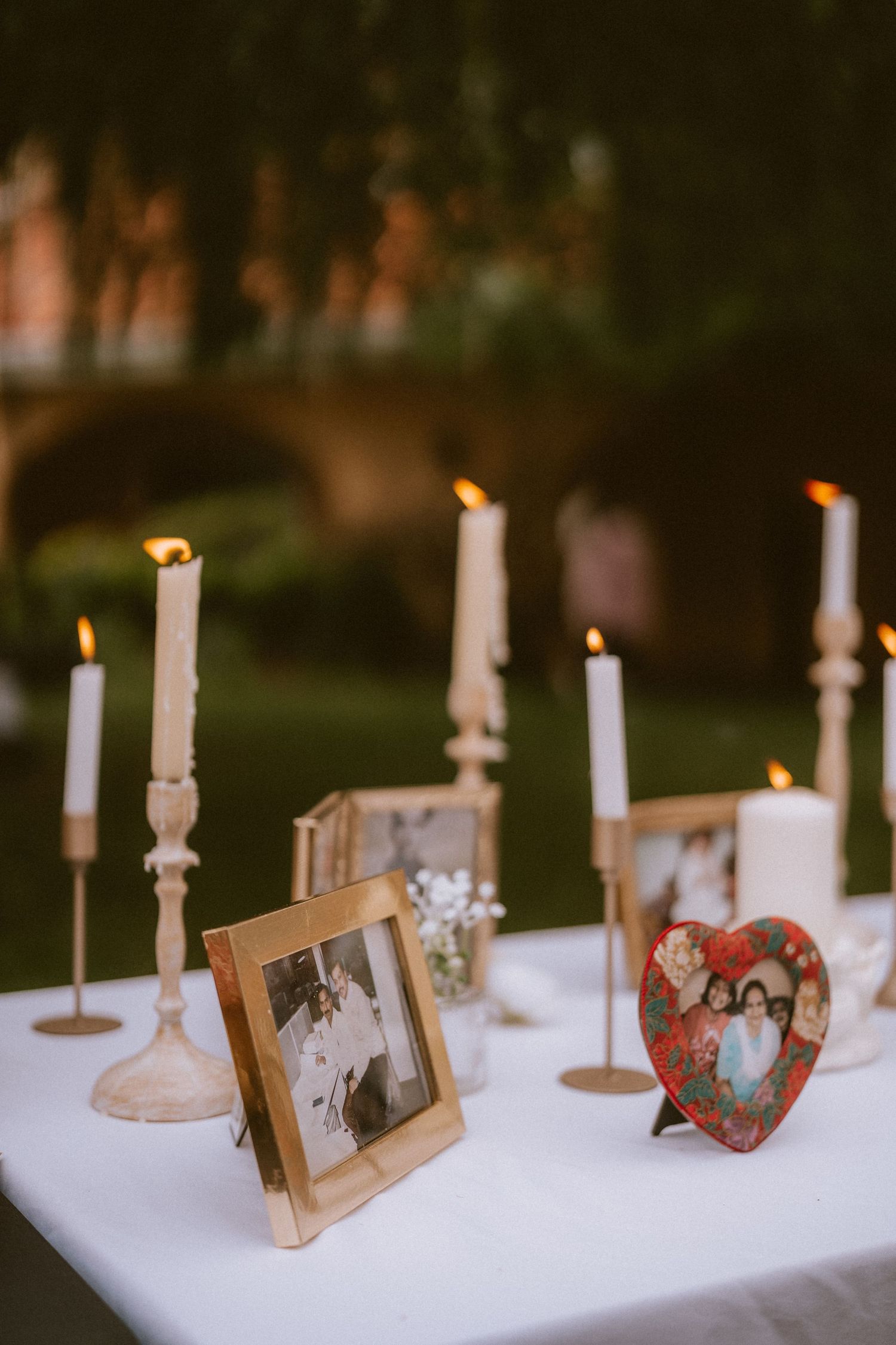 White candles and vintage photo frames create a romantic memorial display on a white tablecloth.