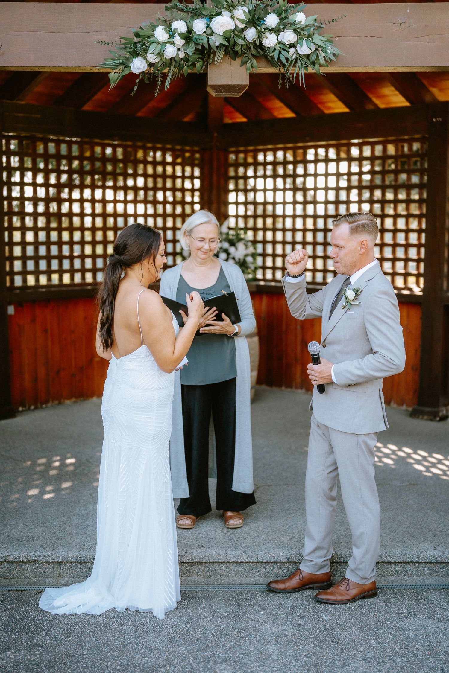 First look wedding photos captured under a wooden pergola with white floral arrangements.