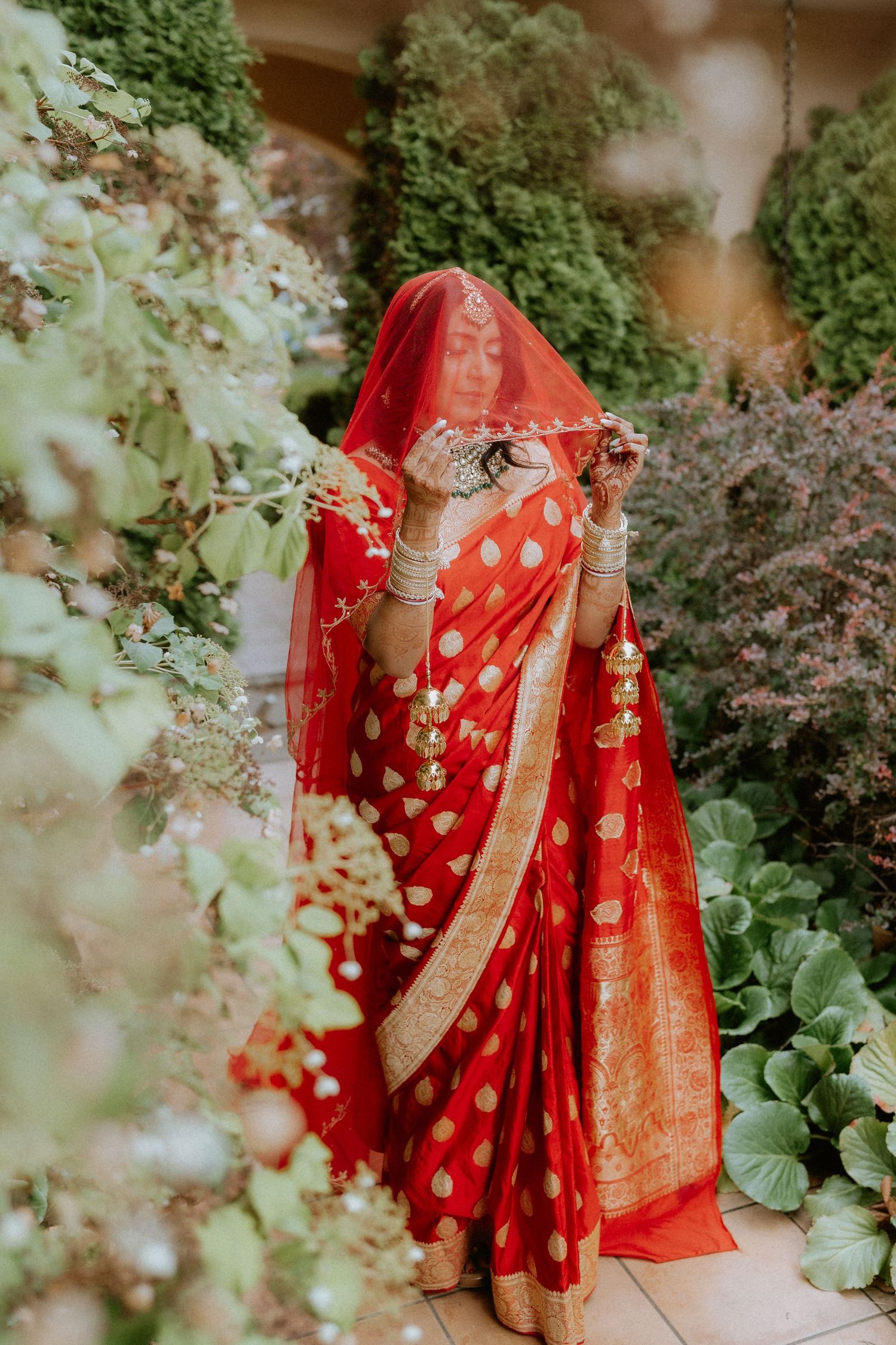 A bright red and gold traditional Indian saree with polka dots stands elegantly in a lush garden setting.