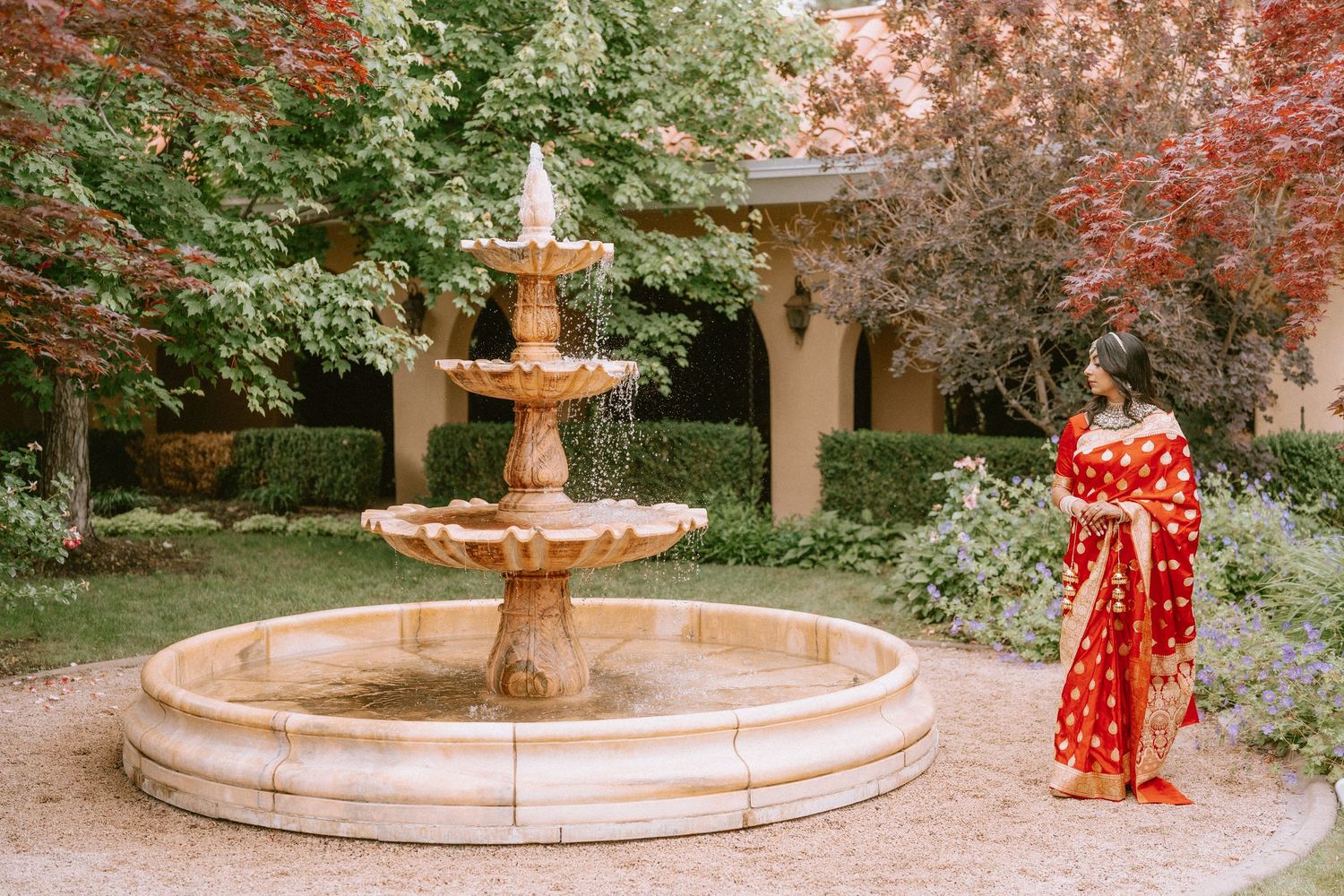 A stone fountain surrounded by pink cherry blossom trees in a serene garden setting during springtime.