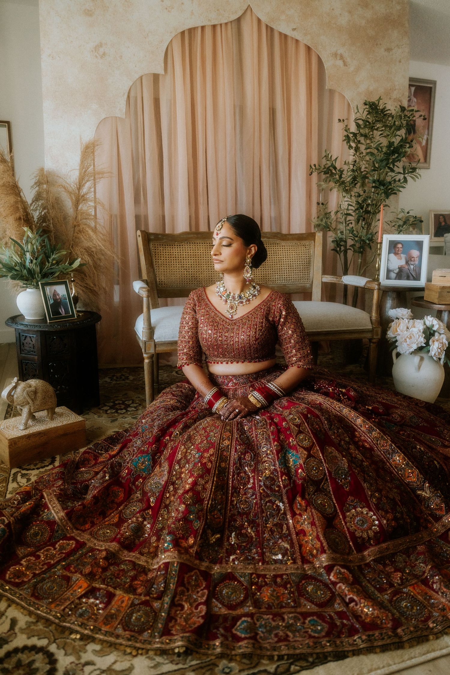 A stunning red and gold embroidered lehenga dress is showcased in multiple angles against a neutral interior setting.