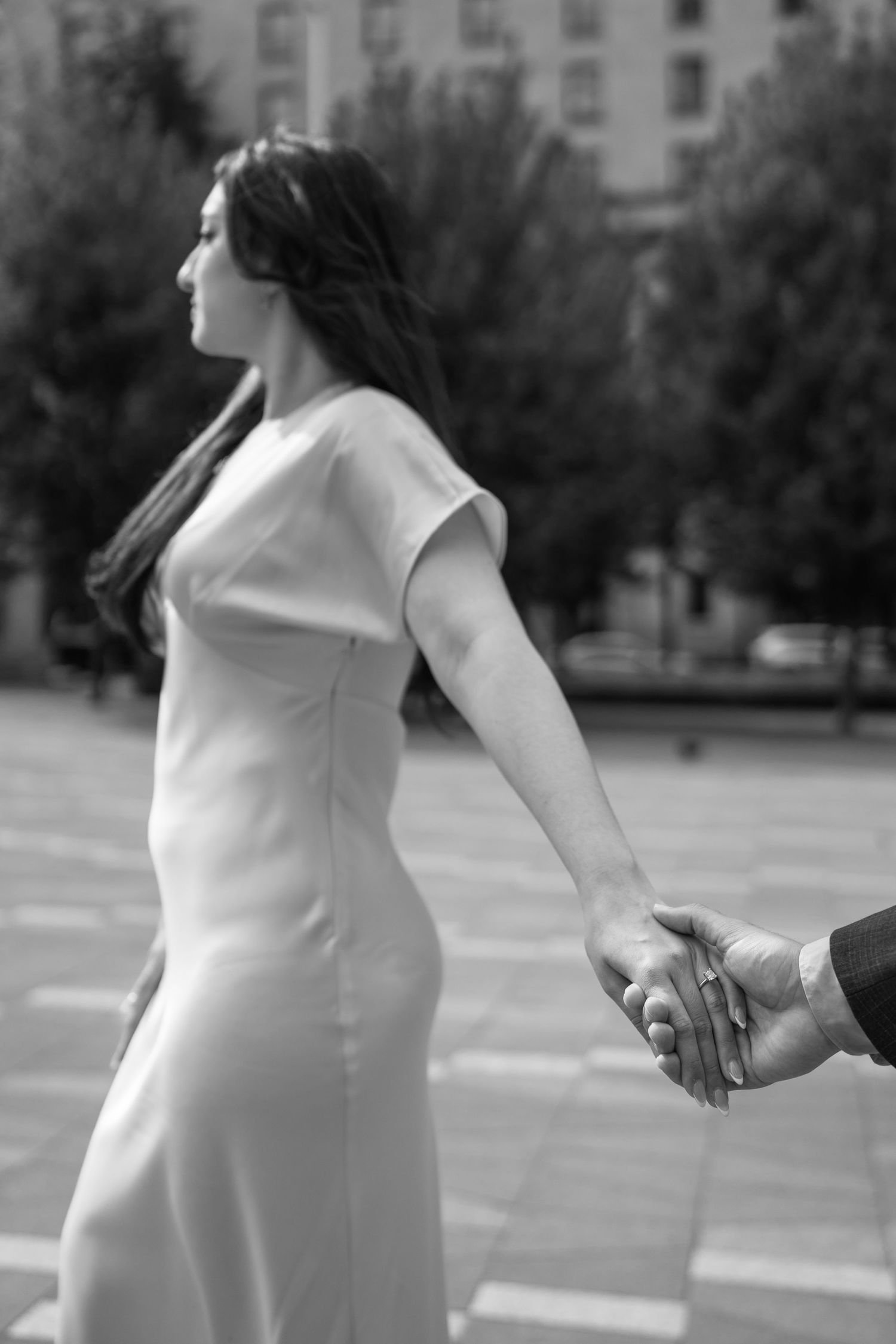 A pregnant woman in a white dress stands in a city street in a black and white photo series.