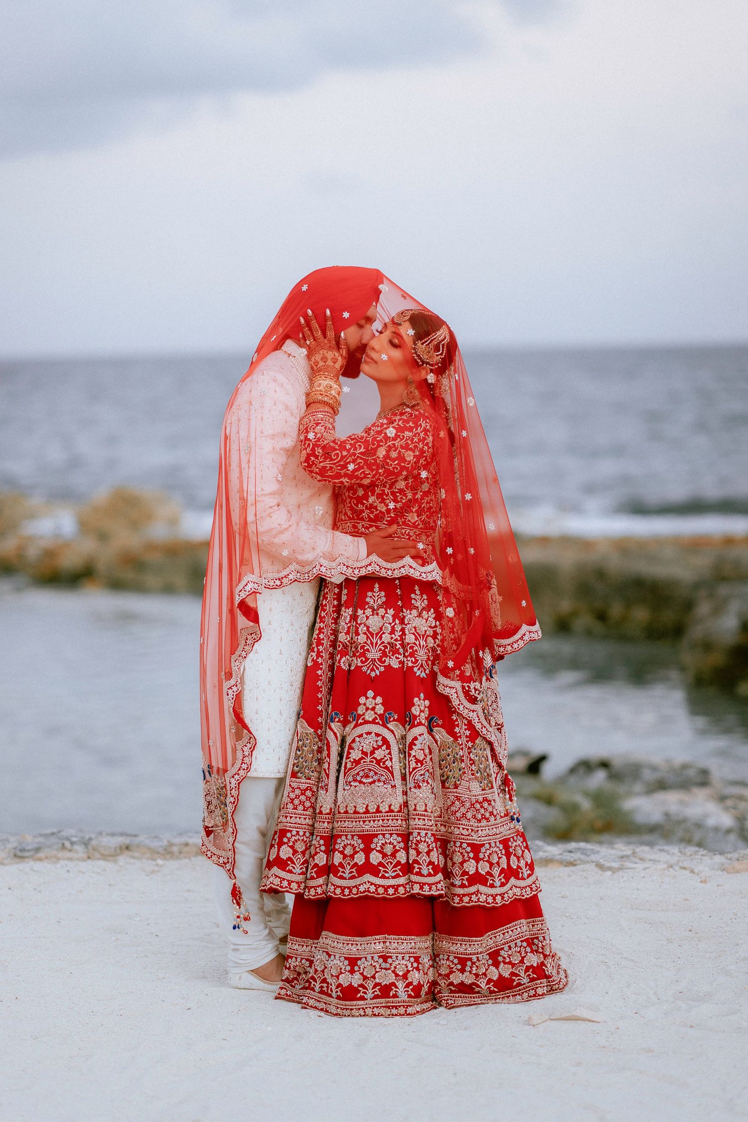 Traditional red and white embroidered Indian wedding lehenga photographed against a misty coastal backdrop.