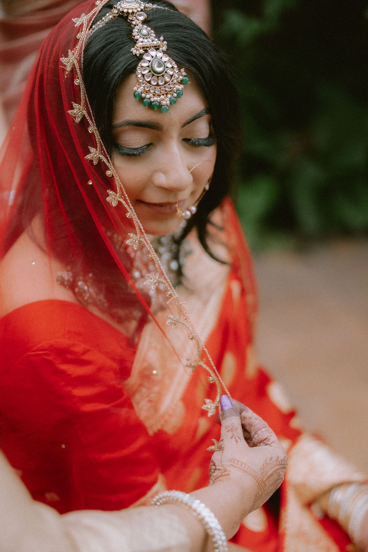 Ornate bridal jewelry and red veil details in traditional South Asian wedding attire.