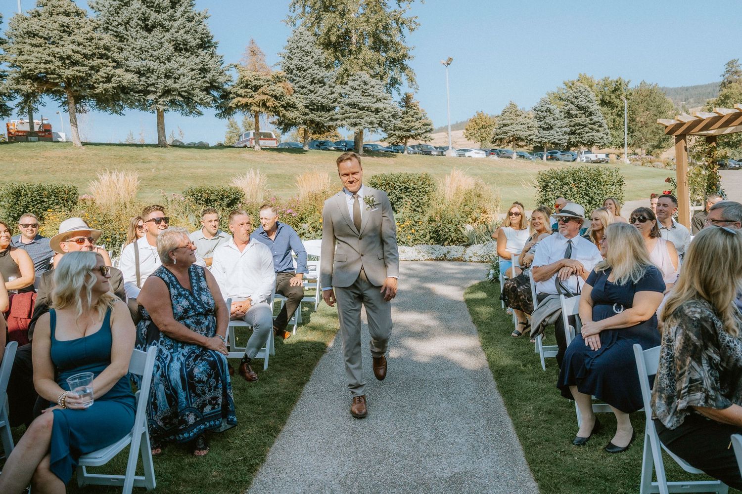 A panoramic view of wedding guests seated outdoors on white chairs during a garden ceremony.
