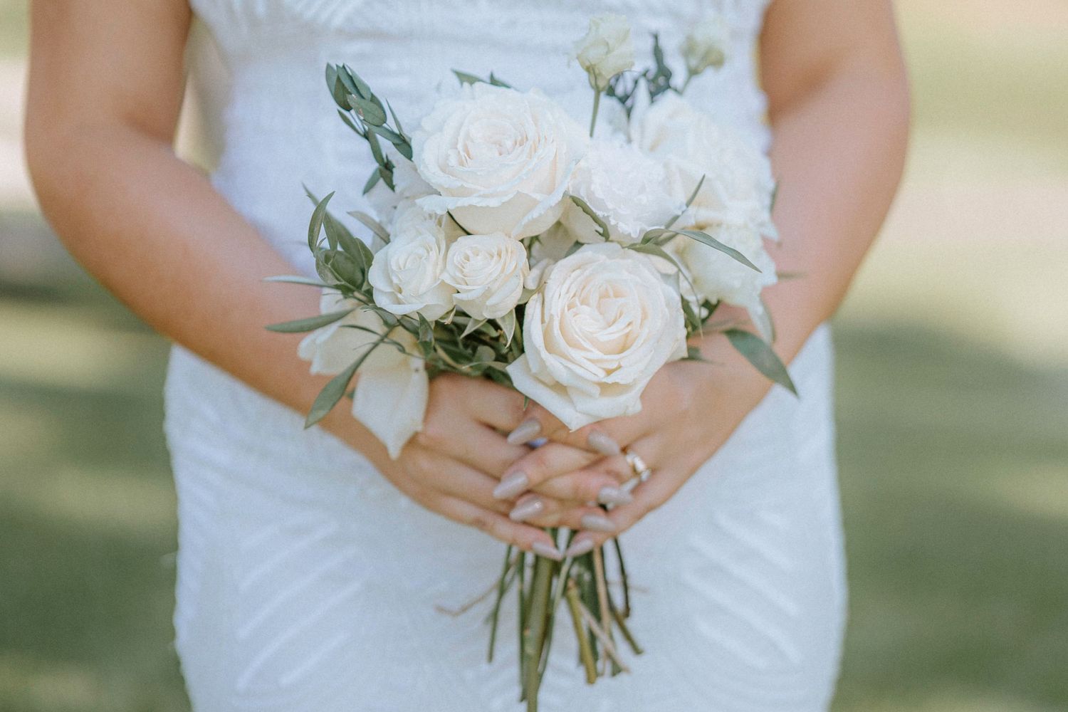 White rose wedding bouquets held against white wedding dresses in natural light.