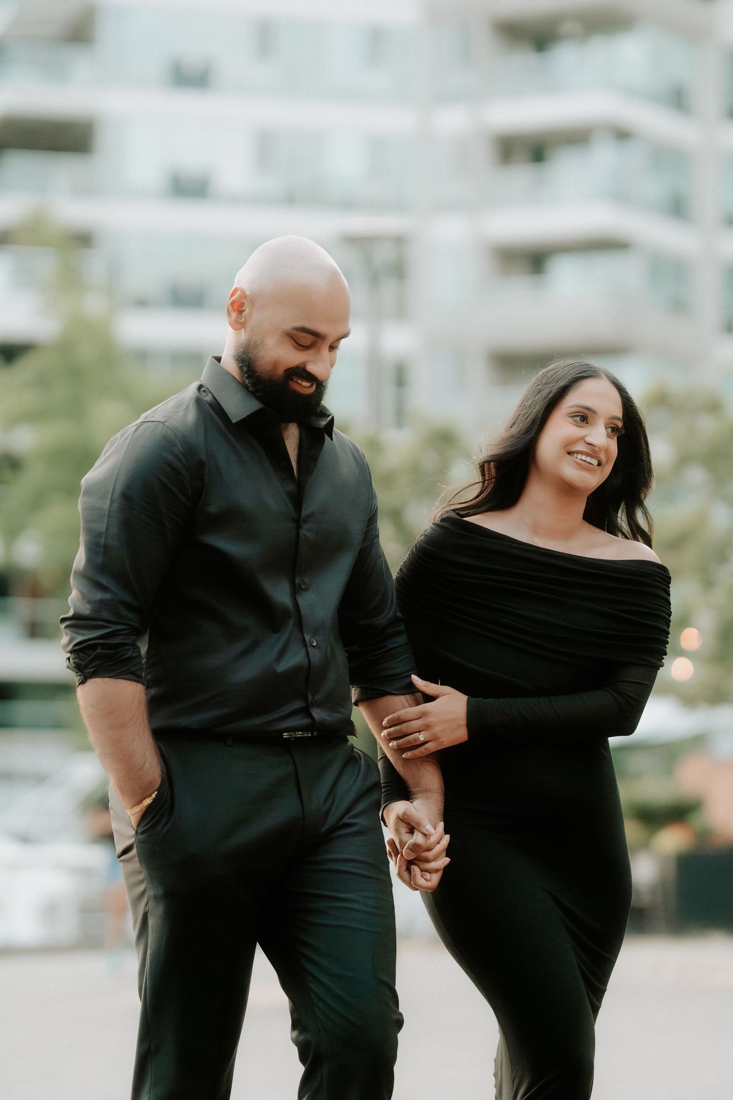 A couple in matching black outfits holds hands and shares intimate moments during an outdoor photo session.