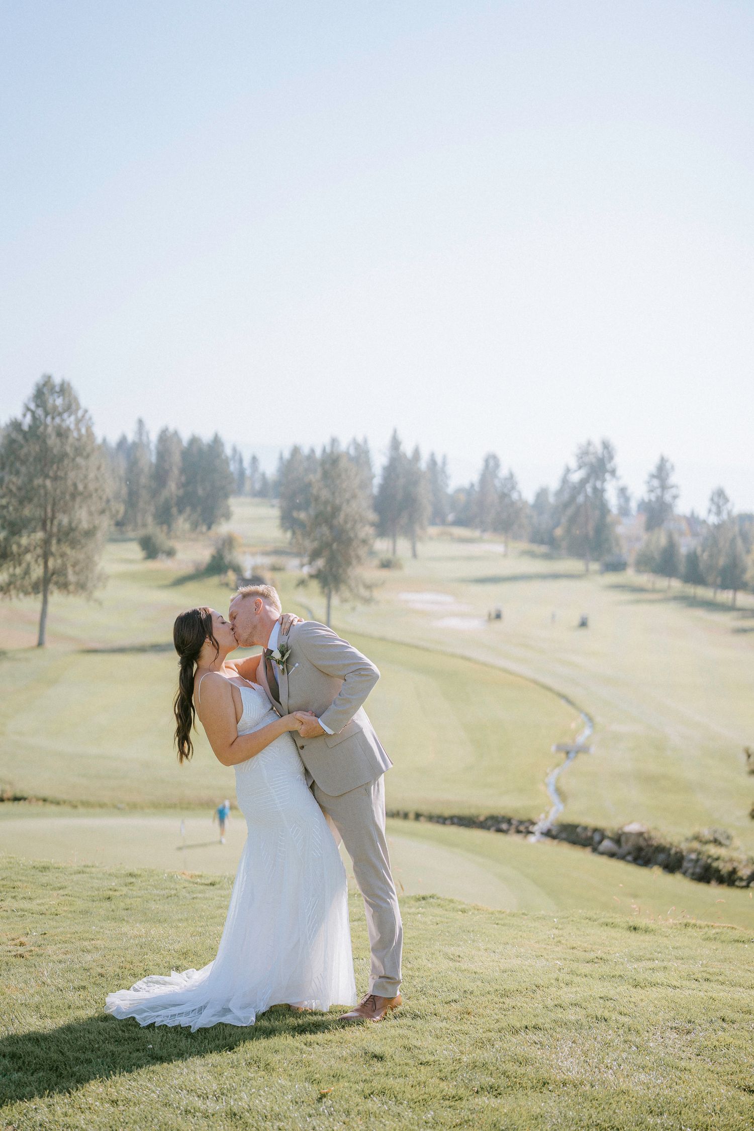 Bride and groom share romantic moments on a sunlit golf course during their wedding photoshoot.