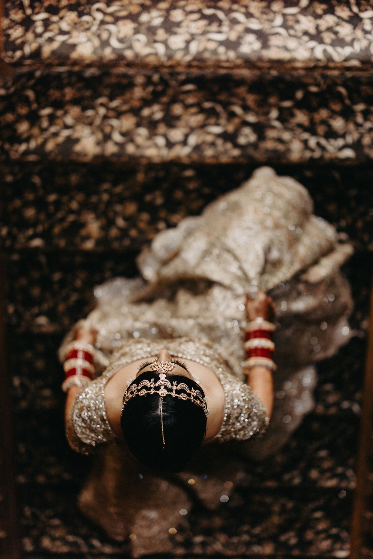 Close-up of traditional Indian bridal hands decorated with henna and bangles on wooden stairs.