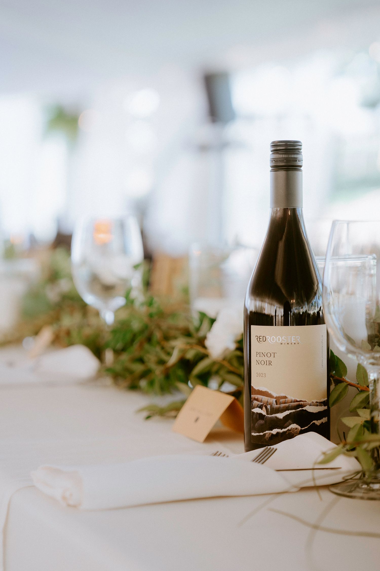 Wine bottles and elegant table settings with greenery decor at a wedding reception.