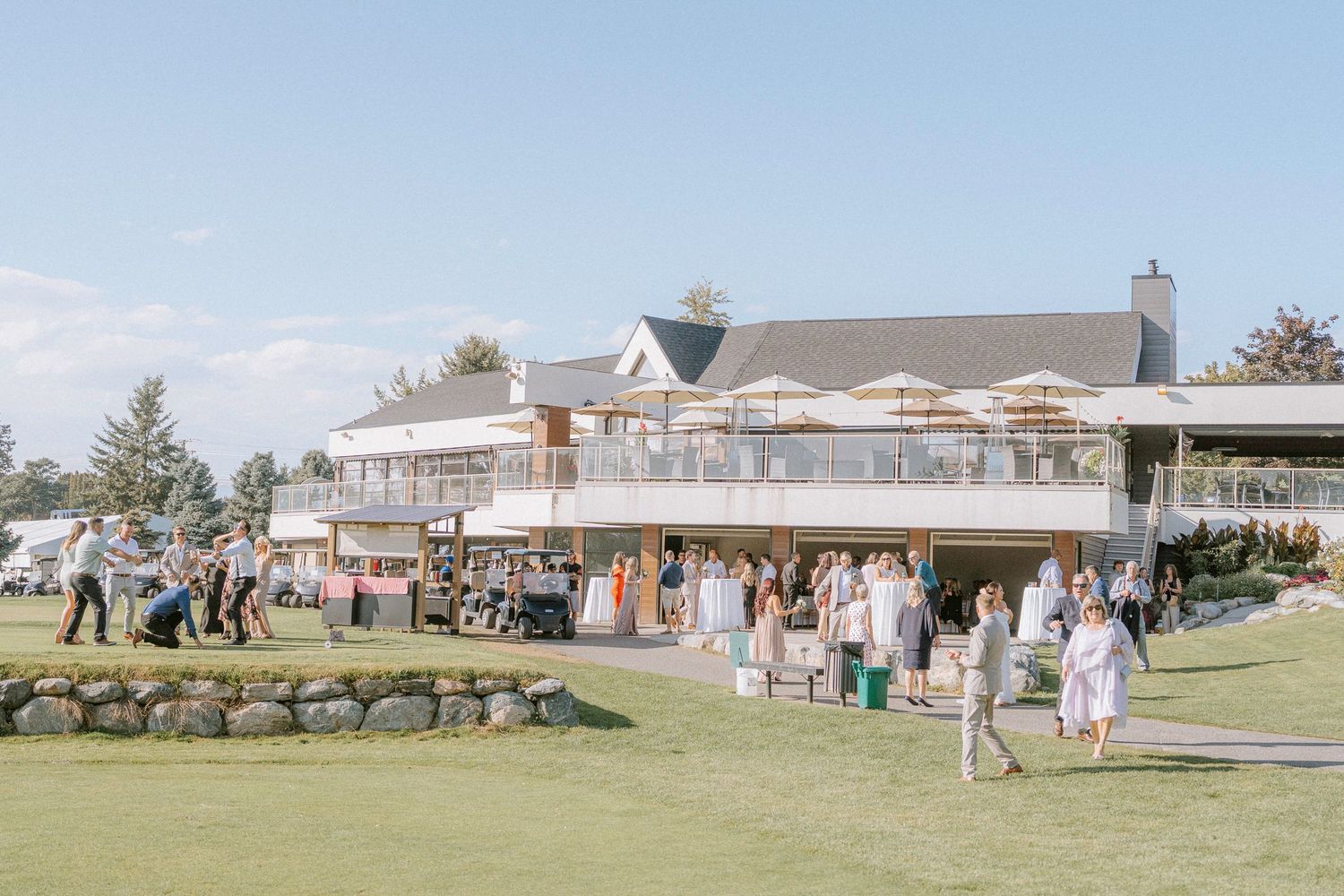 Wedding guests gathering outside an elegant country club building on a sunny day.