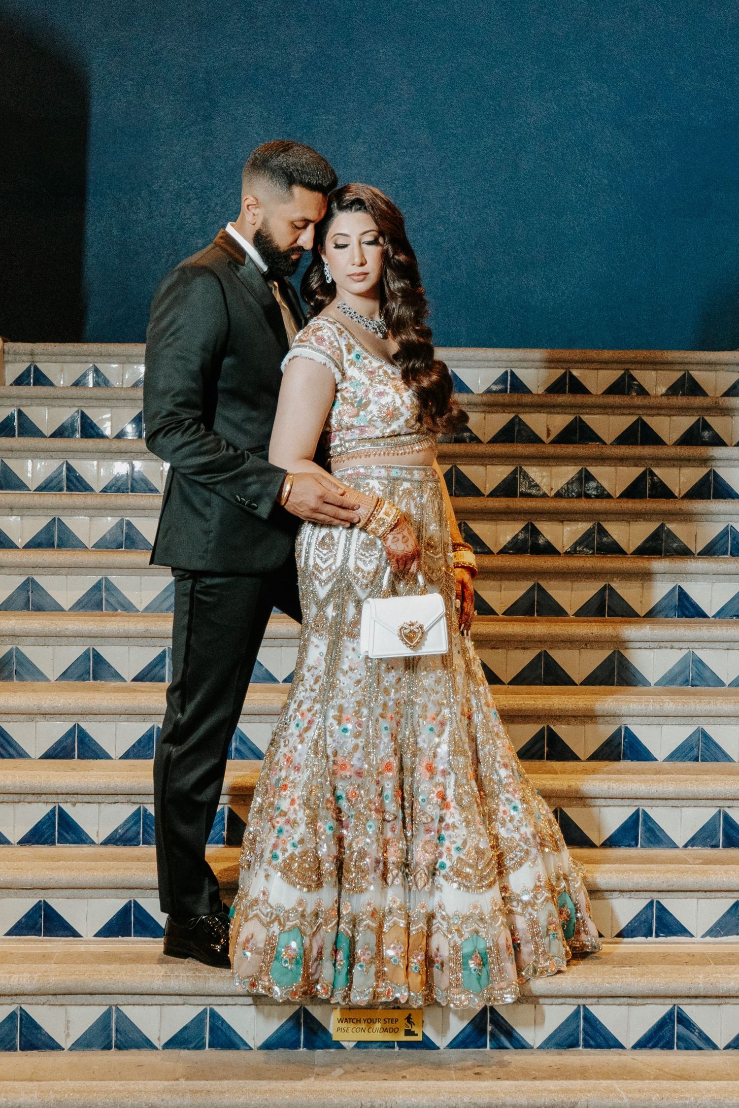 Couple poses on decorative tiled steps in romantic engagement photos with floral dress and dark suit.