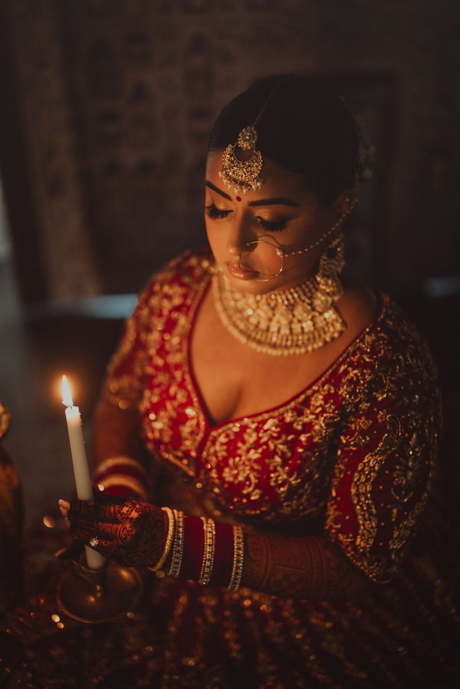 Moody candlelit scene with traditional Indian bridal jewelry and red embroidered lehenga in dim lighting.