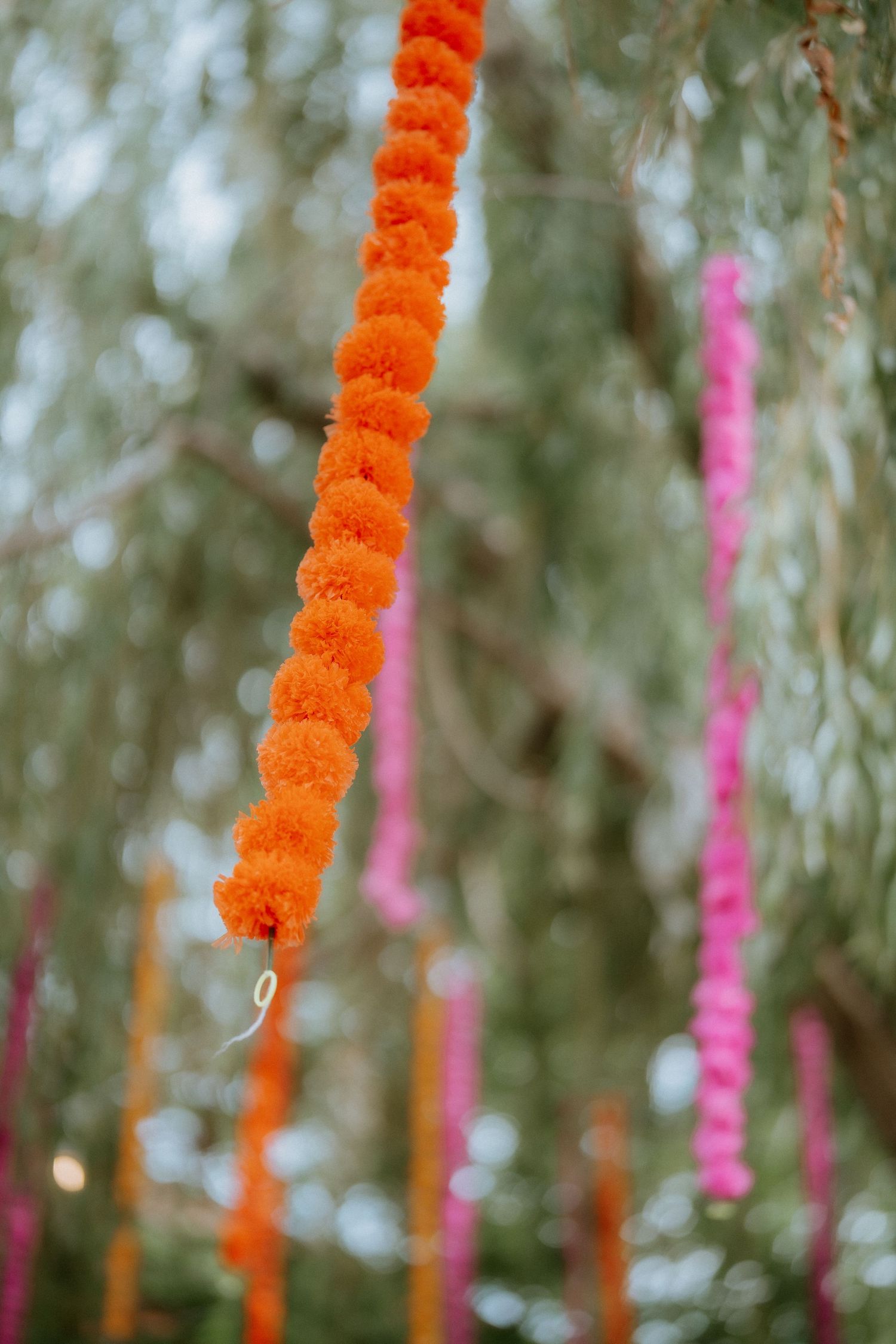 Vibrant orange marigold garlands and pink decorations hang against a soft blurred natural background.