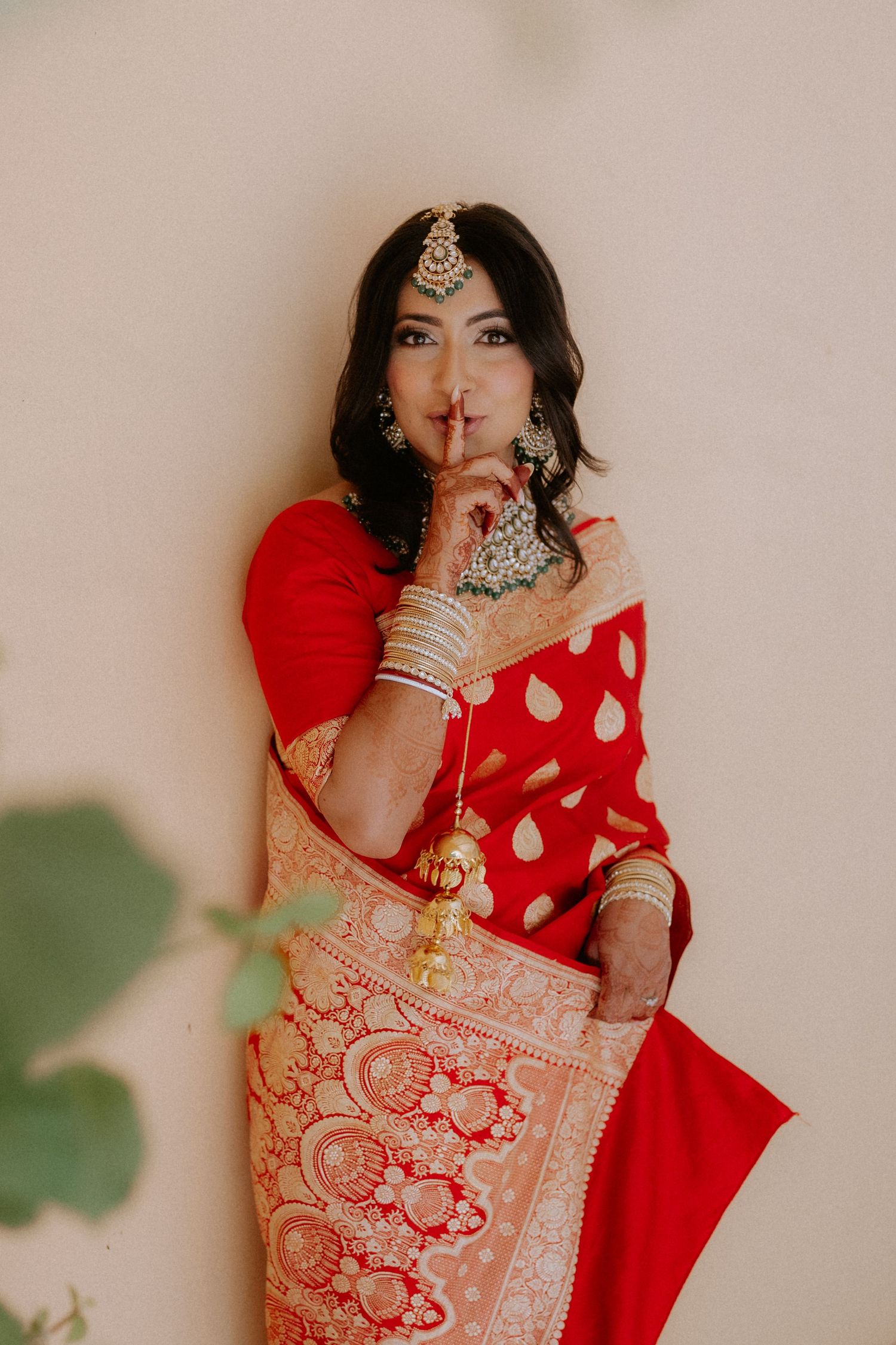 A person in a vibrant red and gold traditional Indian saree making a quiet gesture.