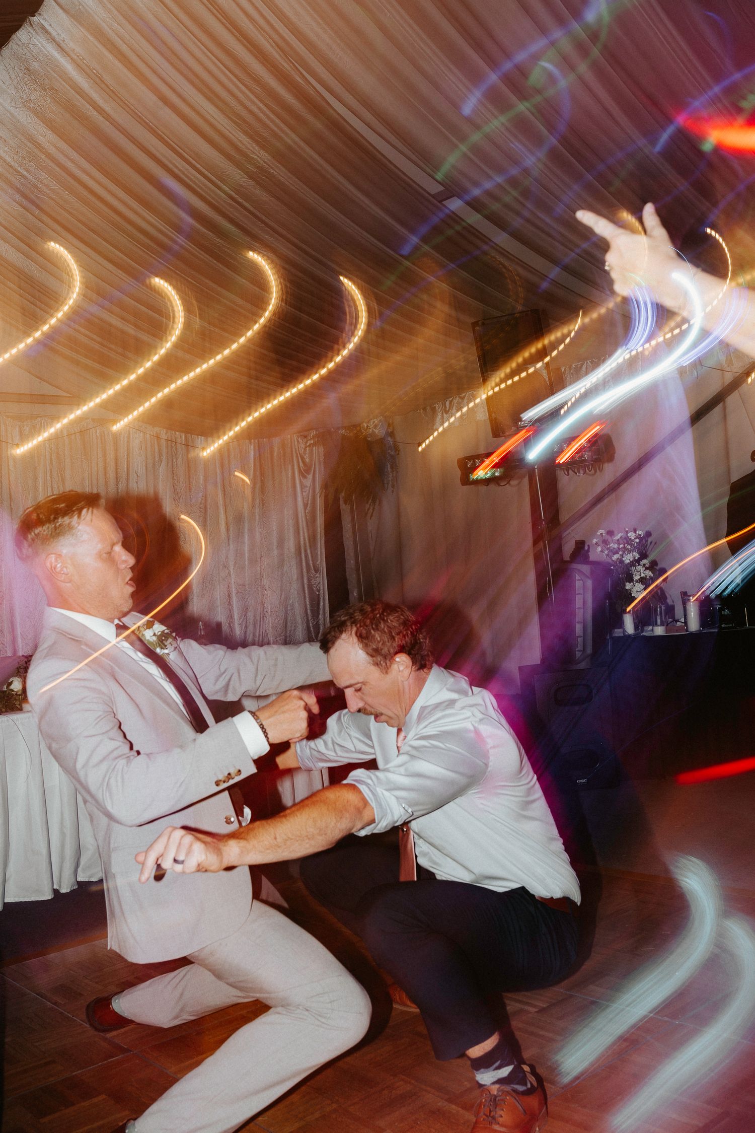 Wedding guests dancing energetically with motion blur effects and colorful lighting on the dance floor.