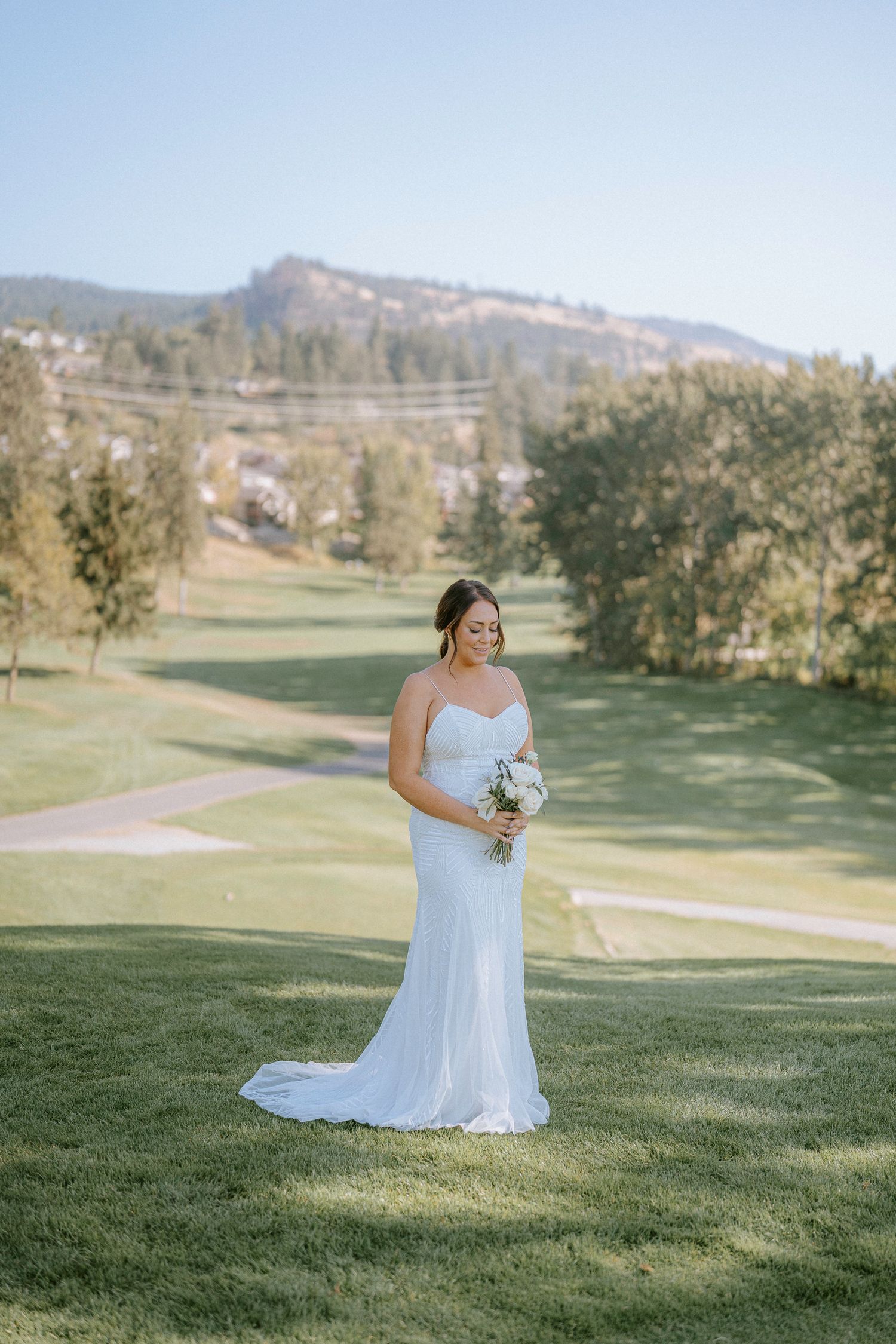 Bride poses for portraits on a scenic golf course with rolling hills and mountains in the background.