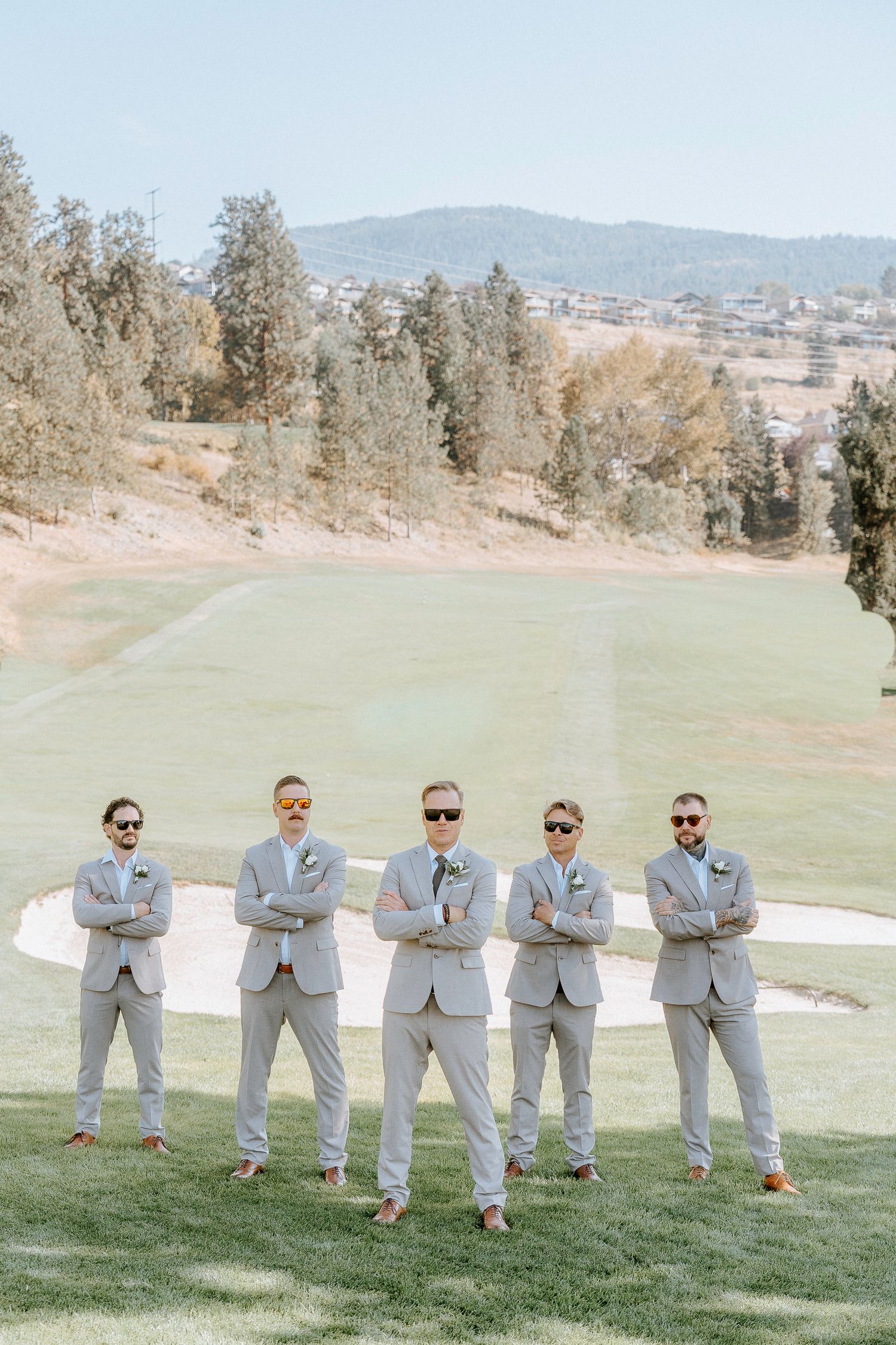 Groomsmen in matching gray suits strike synchronized poses on a grassy golf course.
