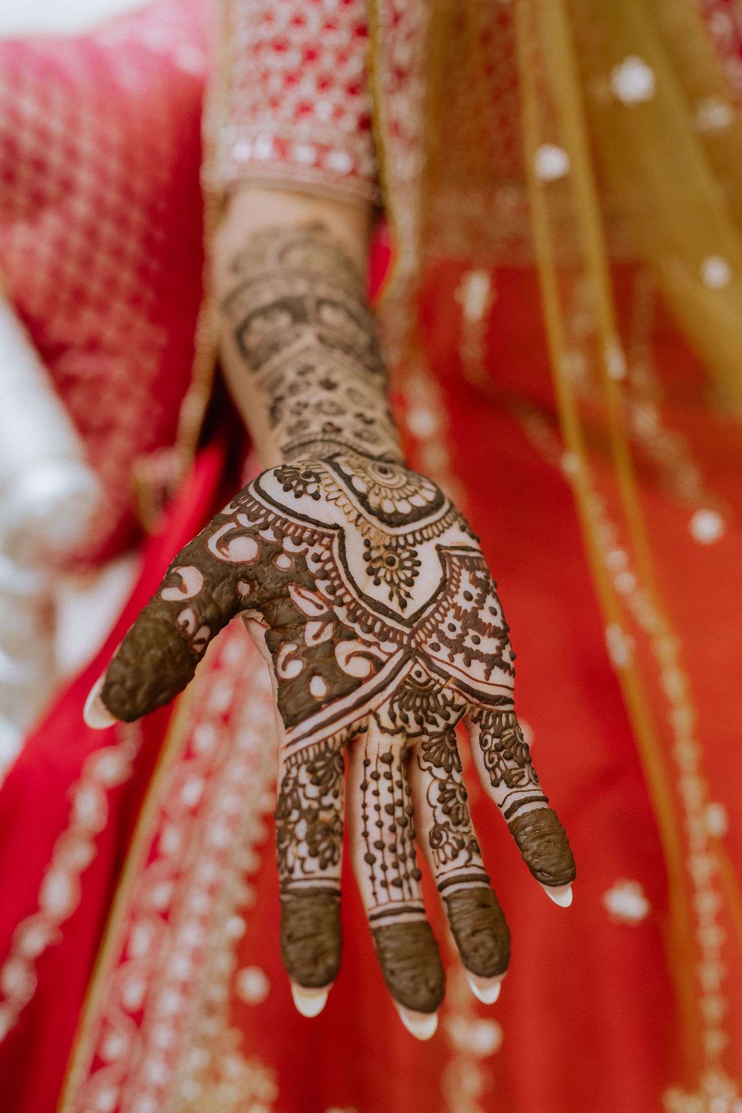 Intricate henna mehndi design adorns a hand against red traditional Indian wedding attire.