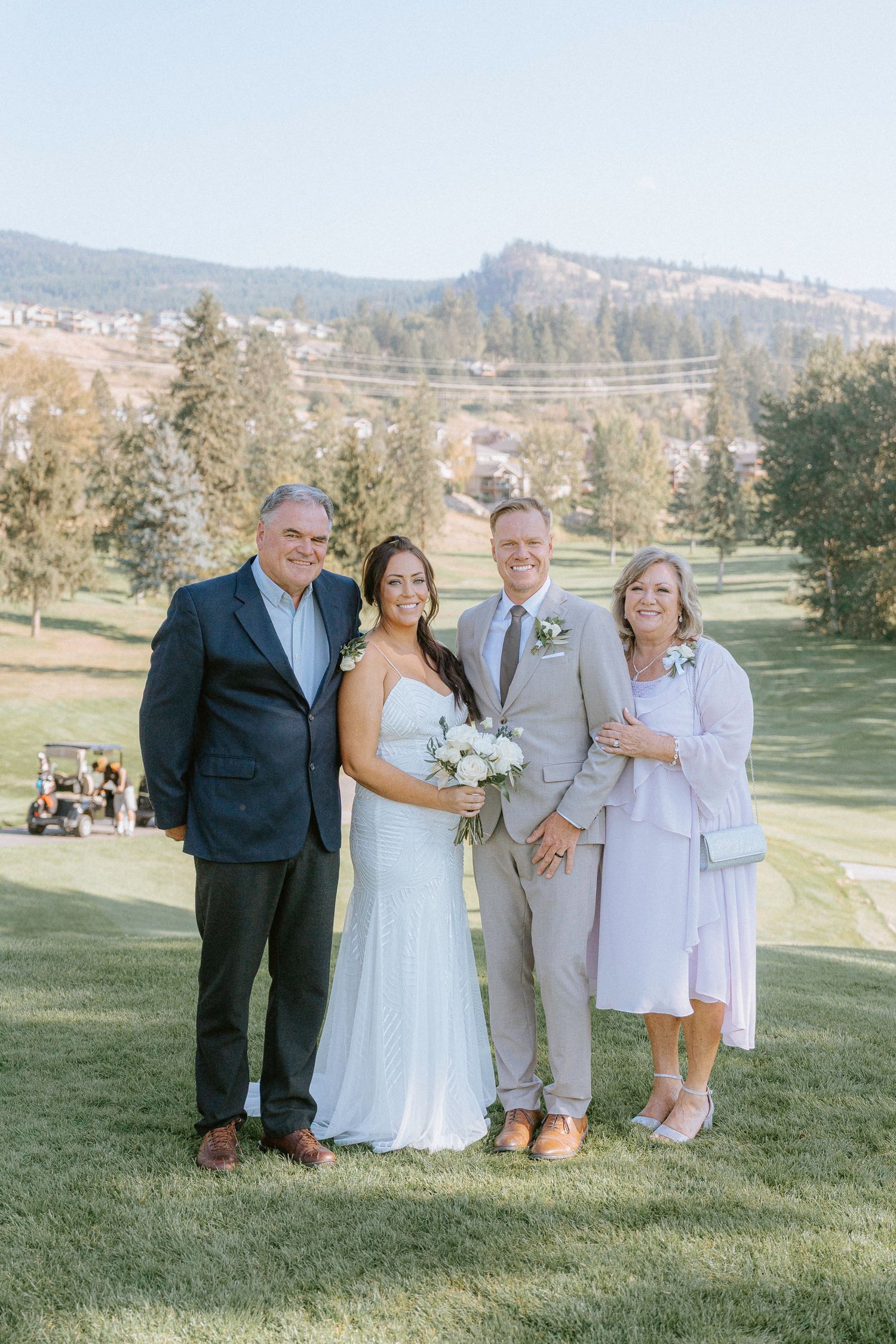Wedding party members pose together on a grassy hill with mountains in the background.