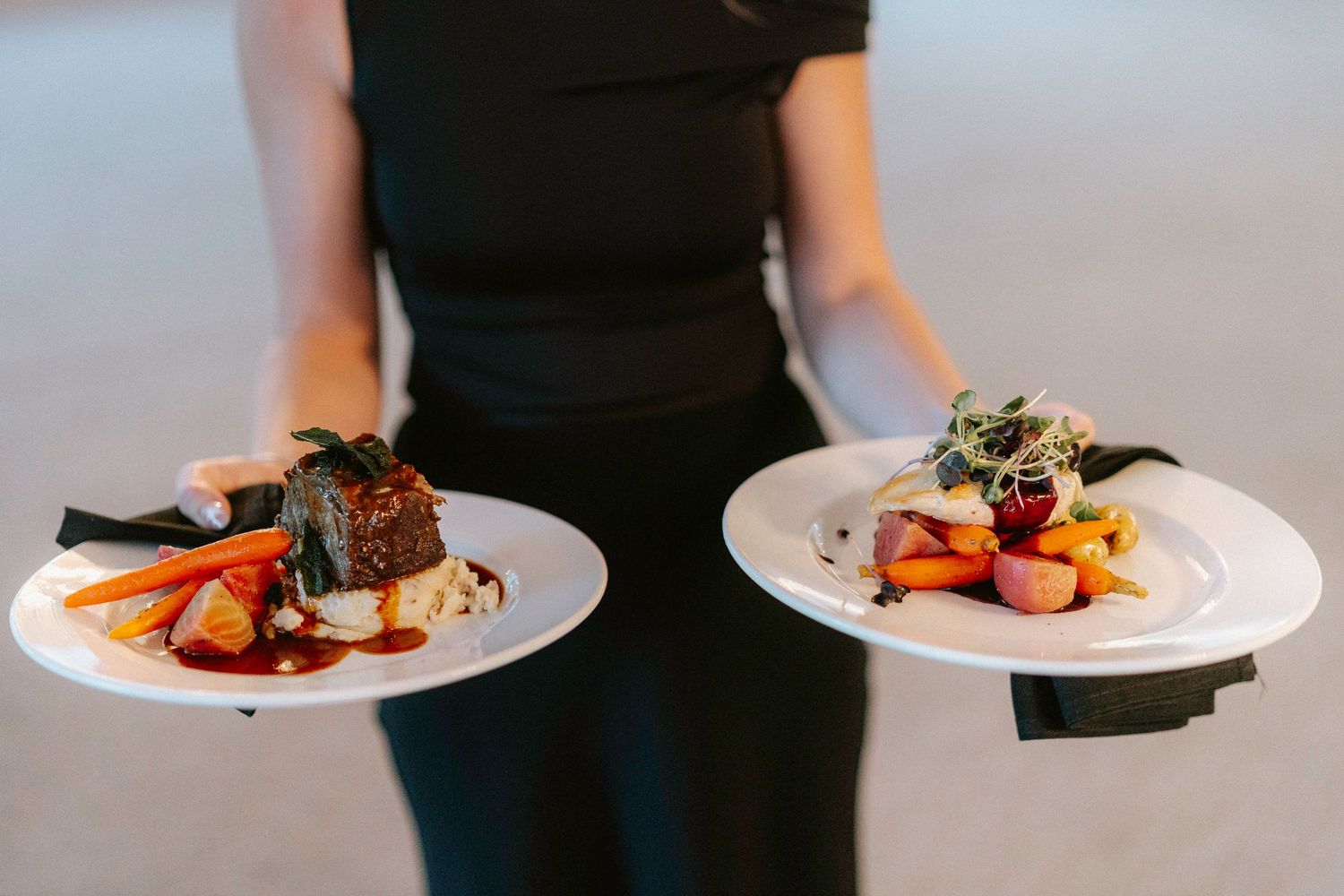Elegant plated meals being served at a wedding reception by staff in black attire.