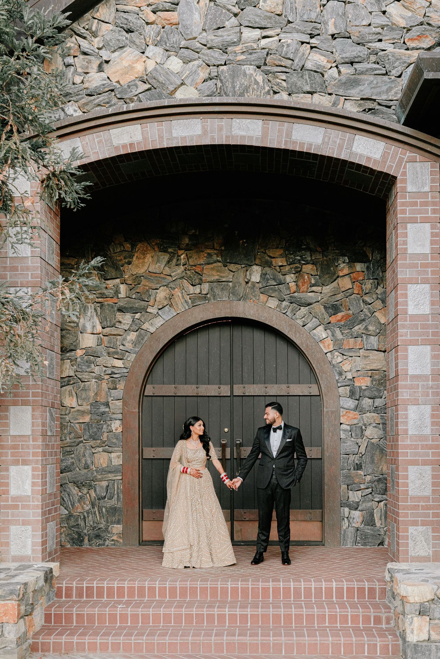 Elegant couple standing in arched stone and brick doorway during wedding photoshoot.