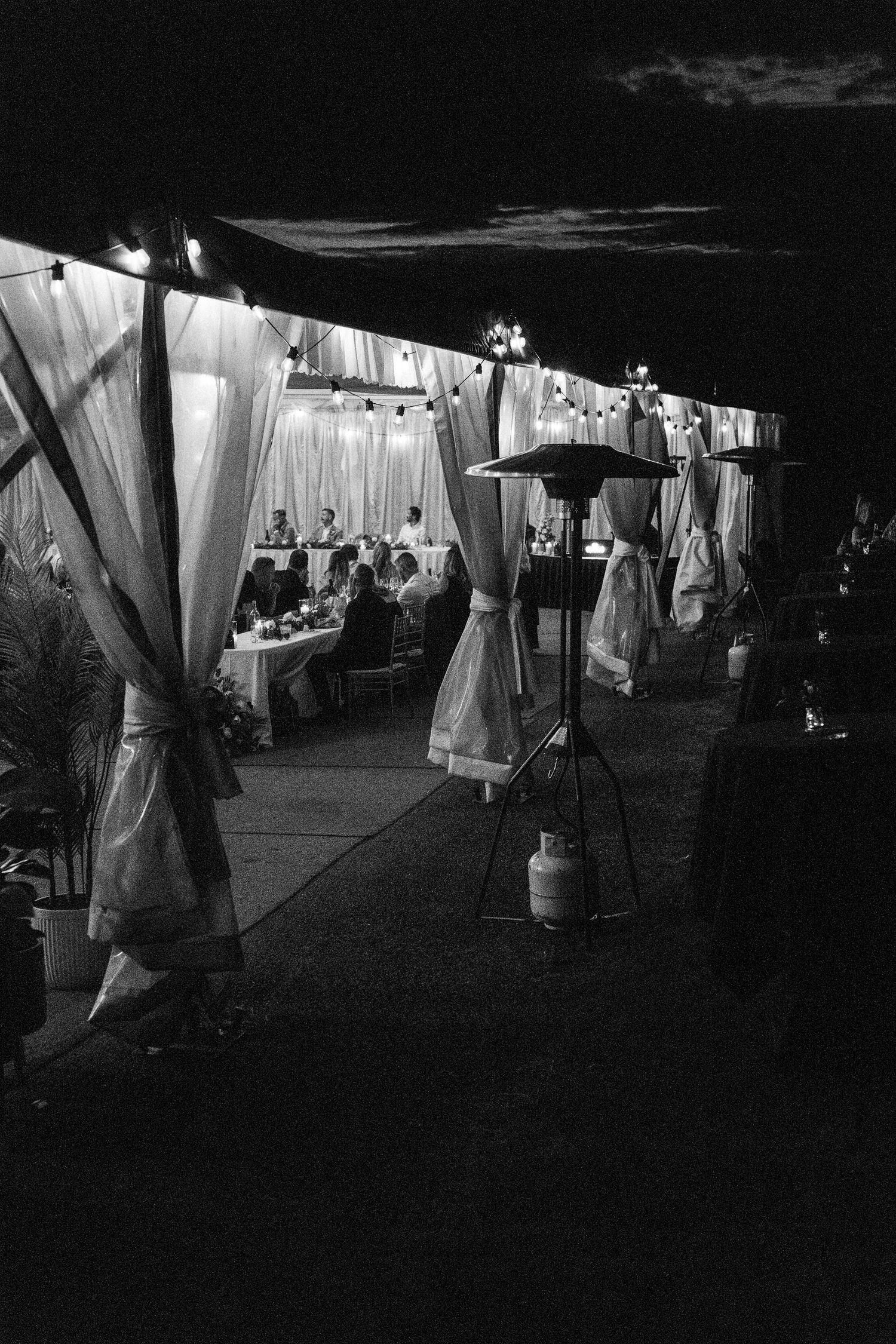 Dark atmospheric shot of a wedding reception tent with white draping and lighting.
