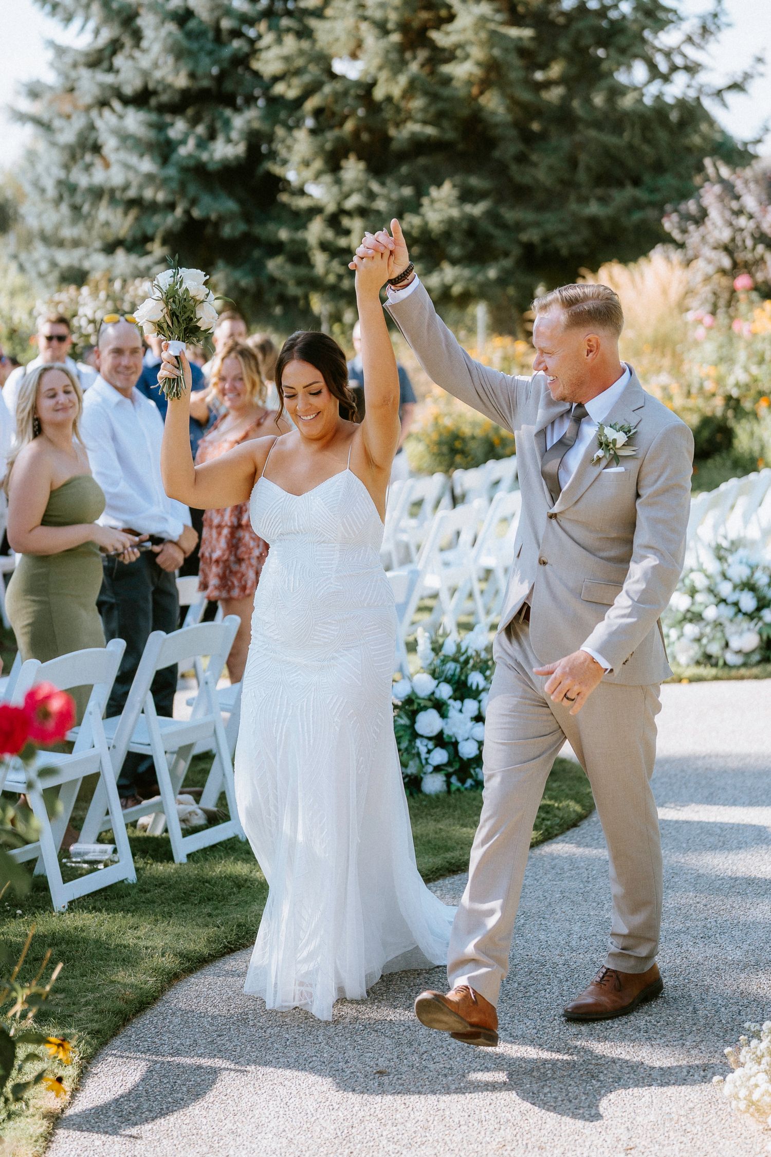 Wedding party dances and celebrates joyfully on an outdoor path surrounded by evergreen trees.