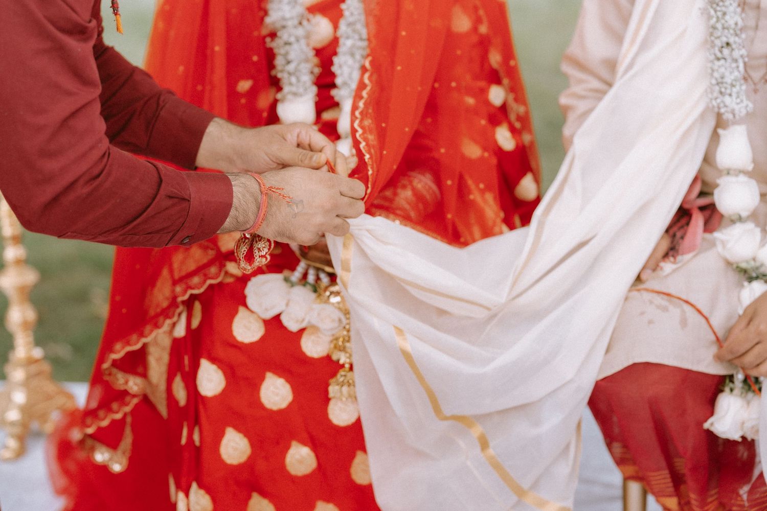 Traditional Indian wedding ceremony showing hands exchanging garlands in vibrant red and white attire.