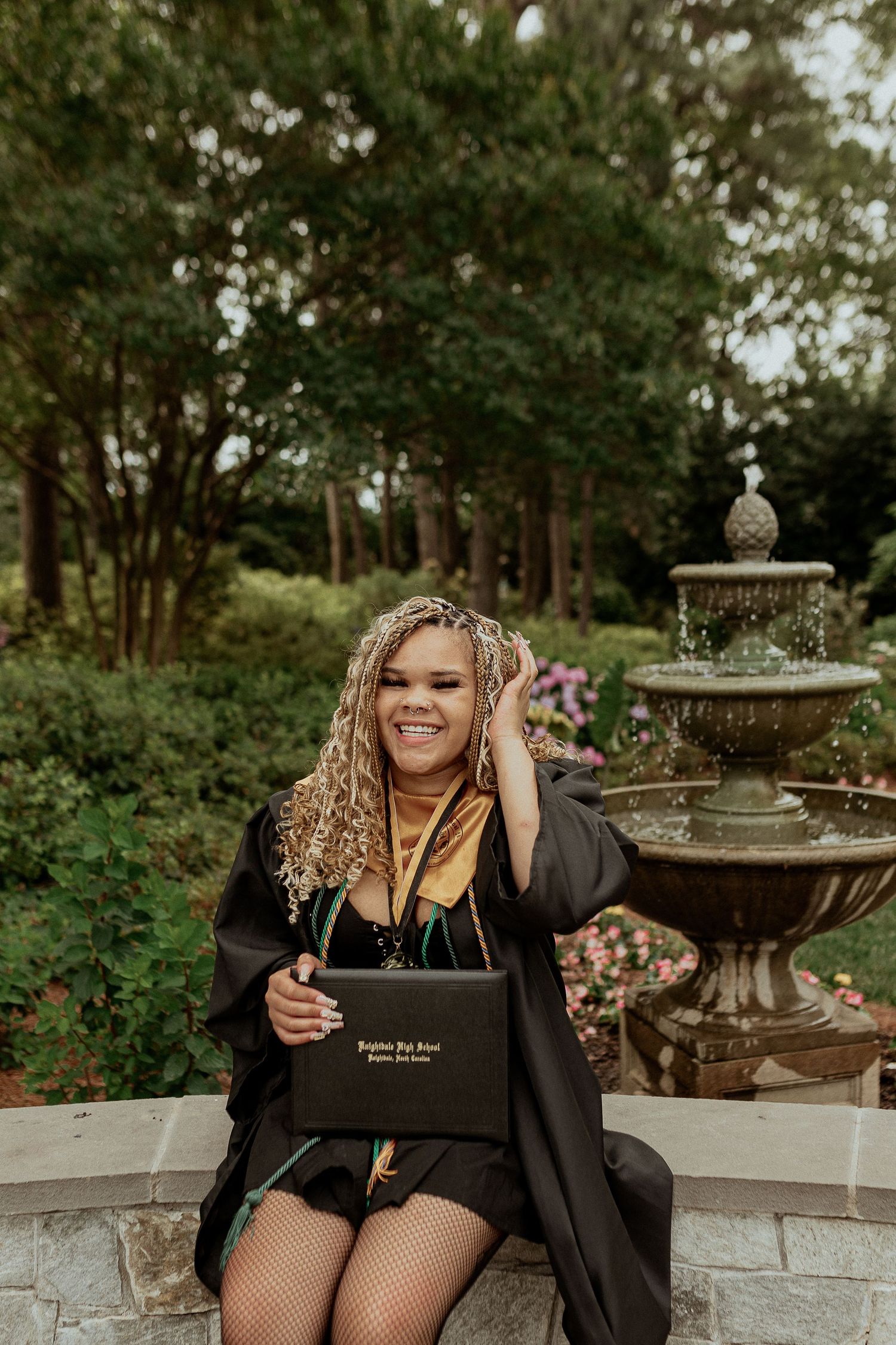 Graduate celebrates on stone steps with water fountain in background.