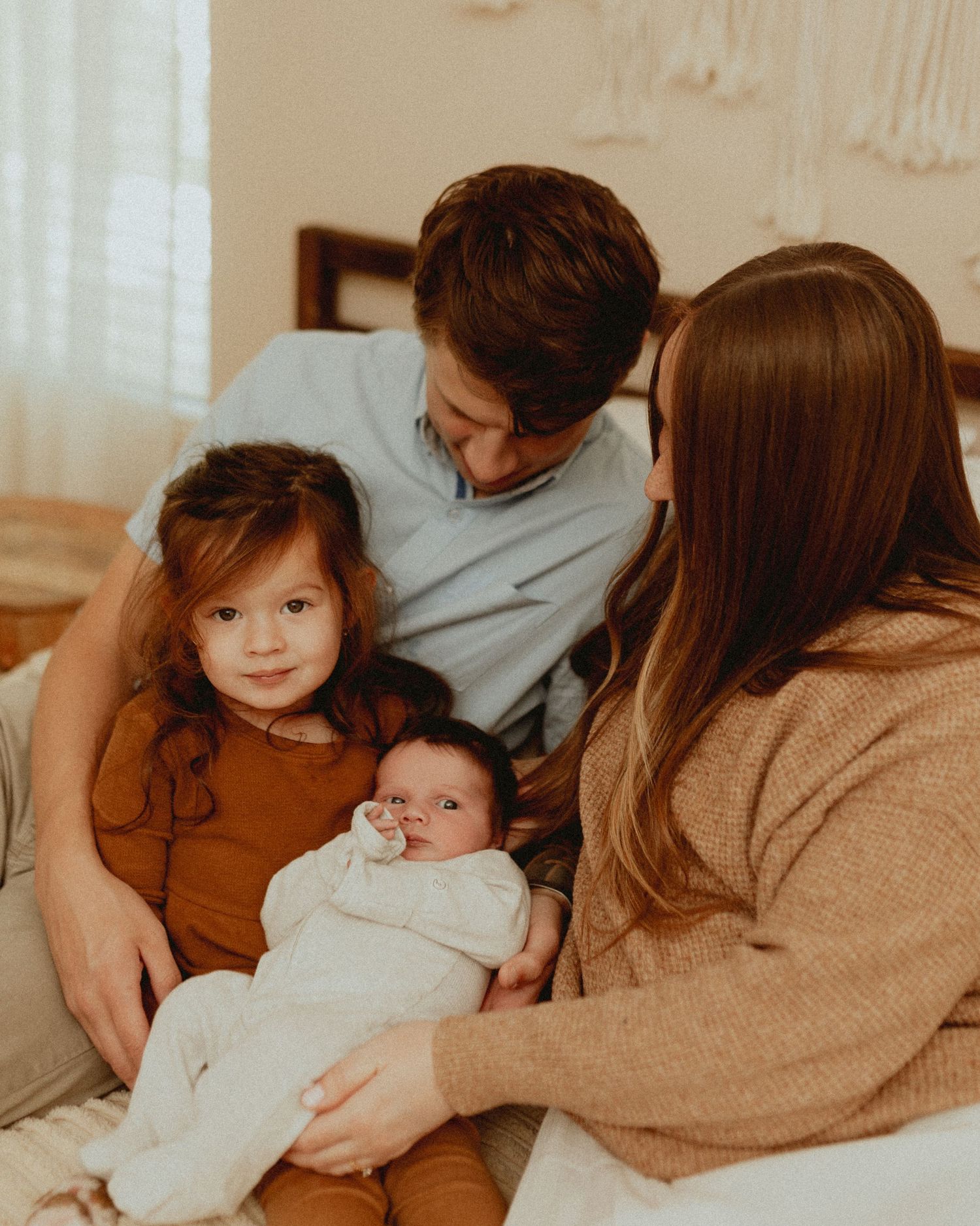 Intimate family moment captured in warm tones as they cuddle together on a bed.