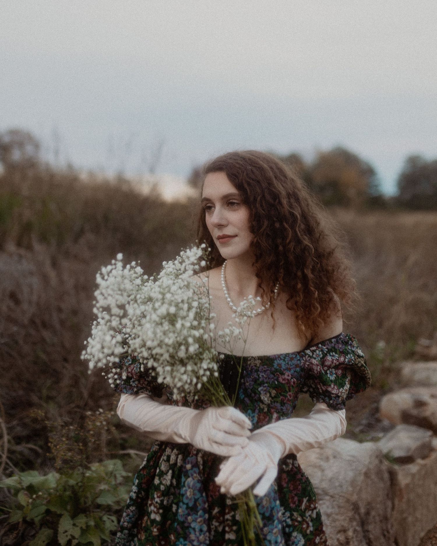Ethereal portrait with baby's breath flowers and flowing floral dress in a dreamy outdoor setting at dusk.