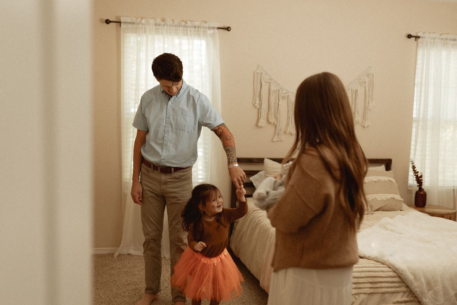 Bright bedroom interior with white curtains and family members spending time together.