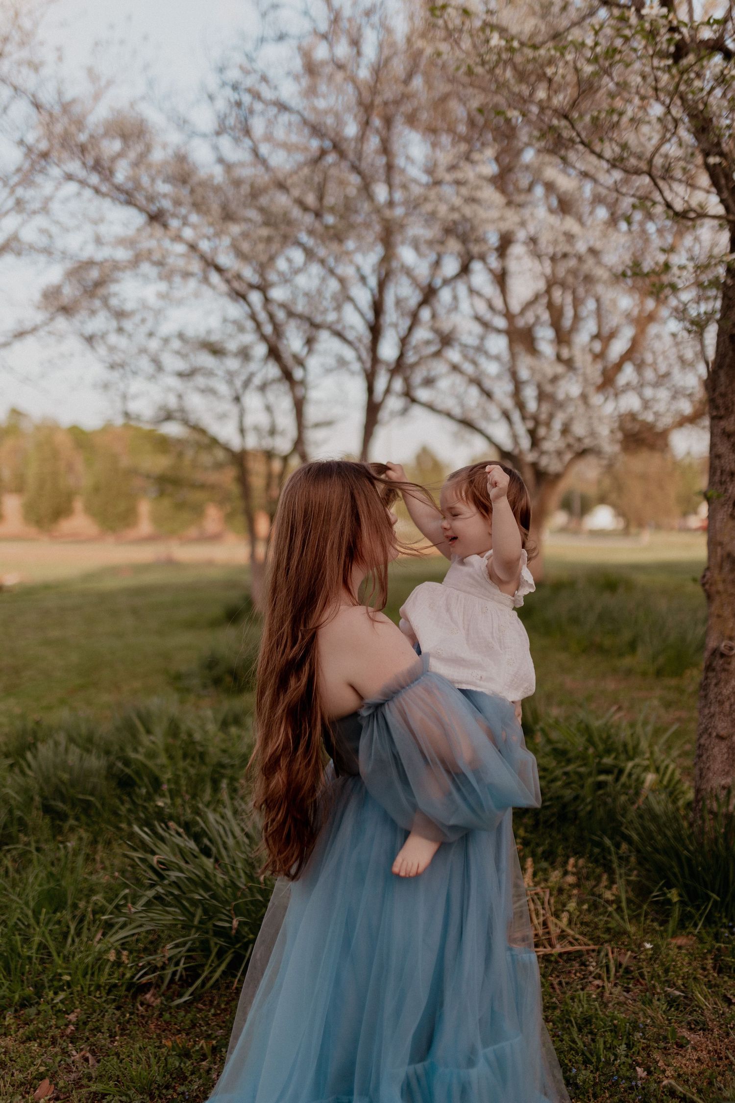 Two people wearing matching blue tulle dresses embrace in a grassy meadow at sunset.