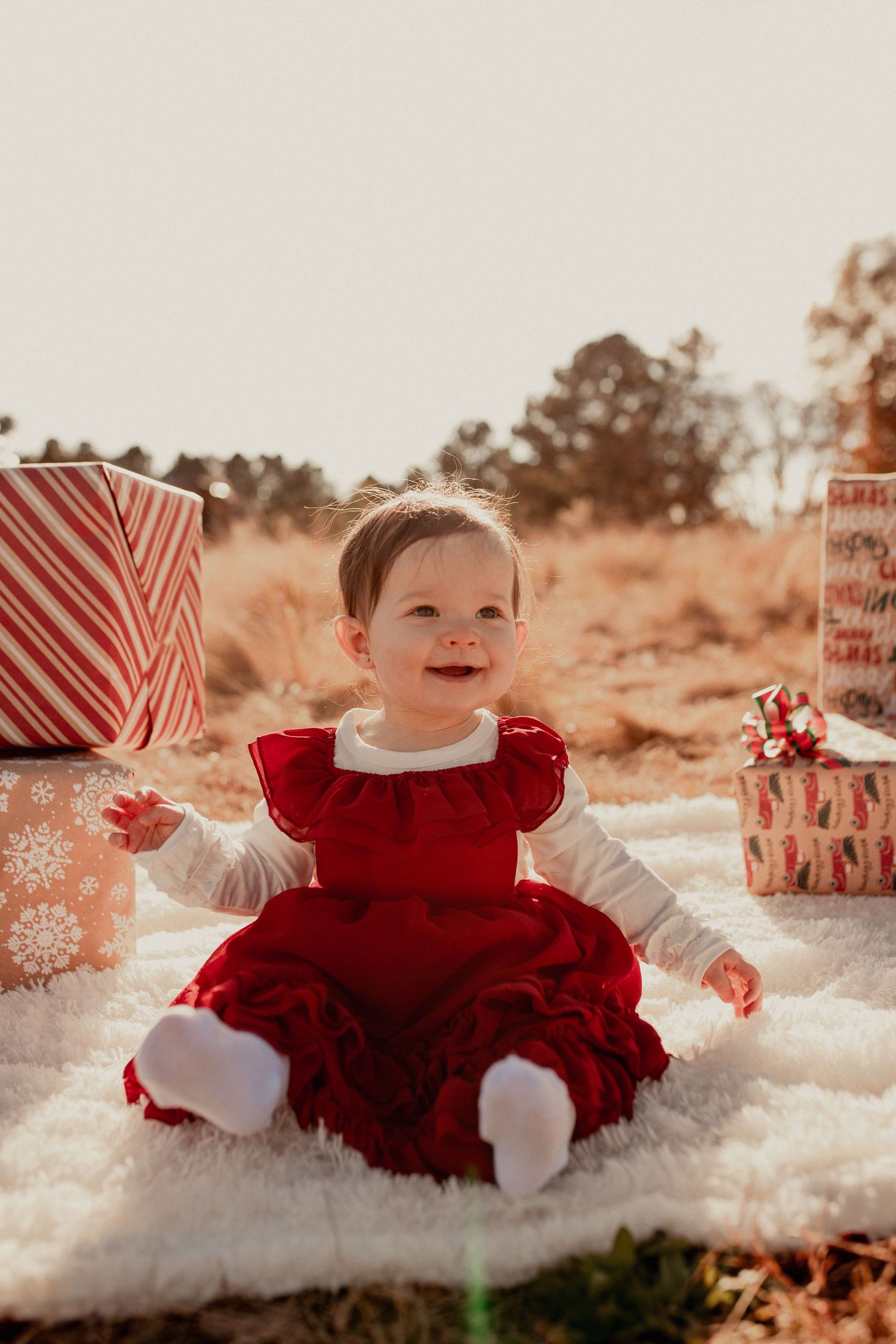 Holiday themed photoshoot with red dress and wrapped presents on faux snow setting.