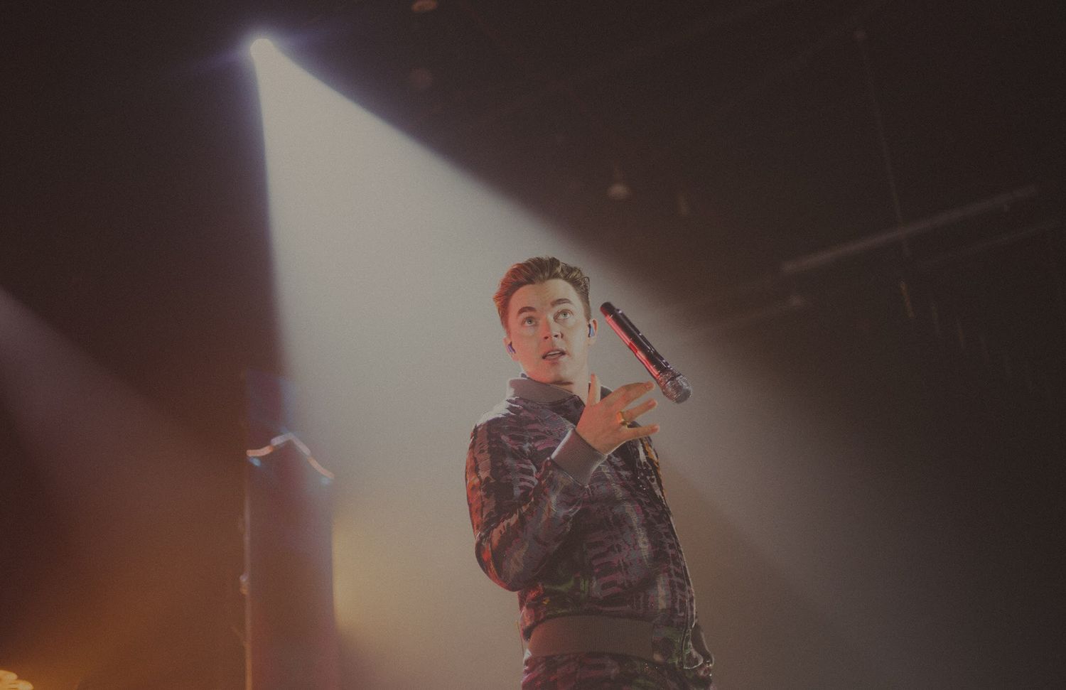 Concert performer silhouetted against bright spotlights in dramatic stage lighting.