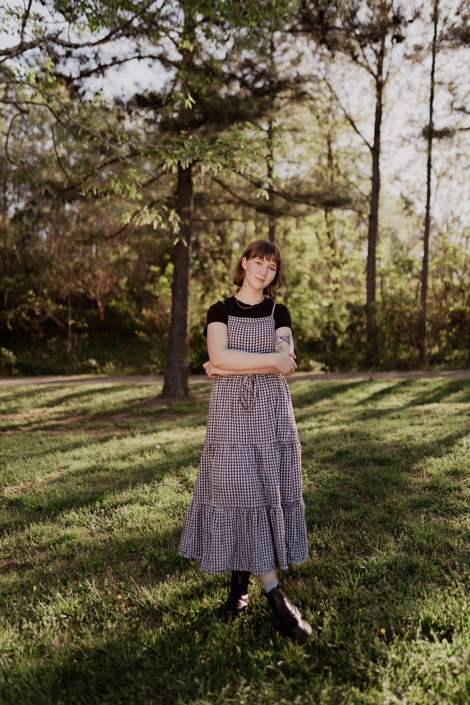 Sunlit outdoor portrait in gingham dress among pine trees.