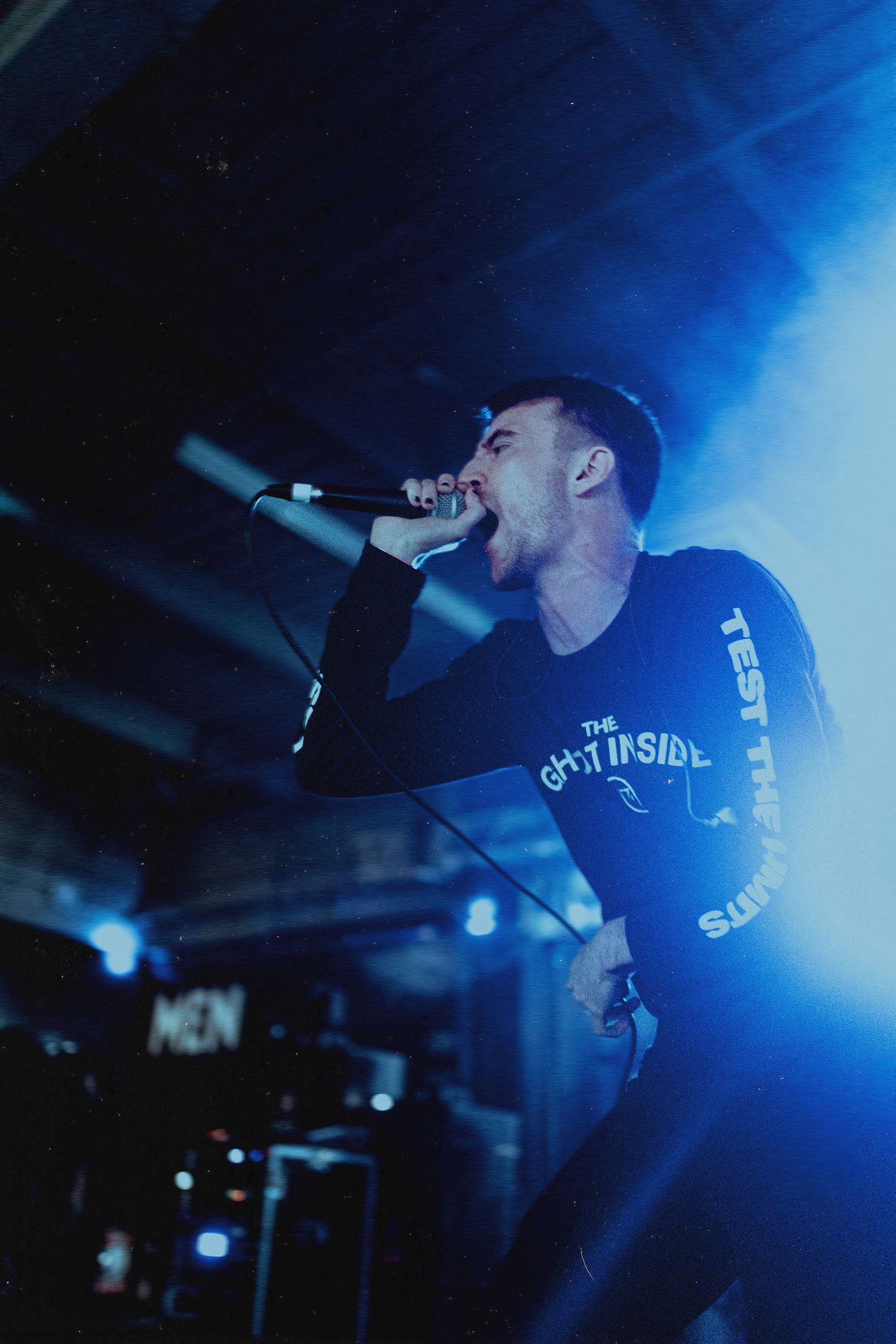 Energetic performer singing into microphone on stage with intense blue lighting.